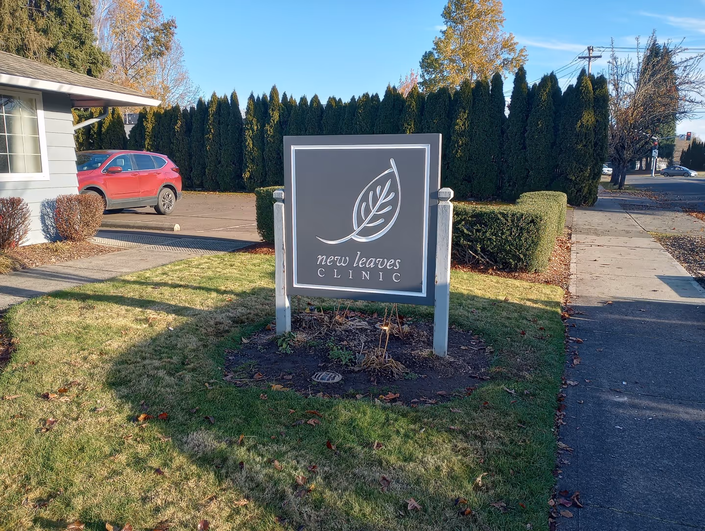 A sign in front of a house with a car parked in the driveway.