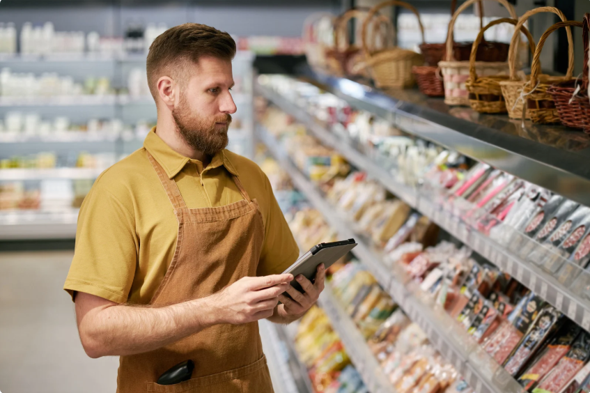 Un épicier utilise une tablette numérique pour la gestion des stocks de charcuterie fine dans un magasin d'alimentation locale à Lyon.