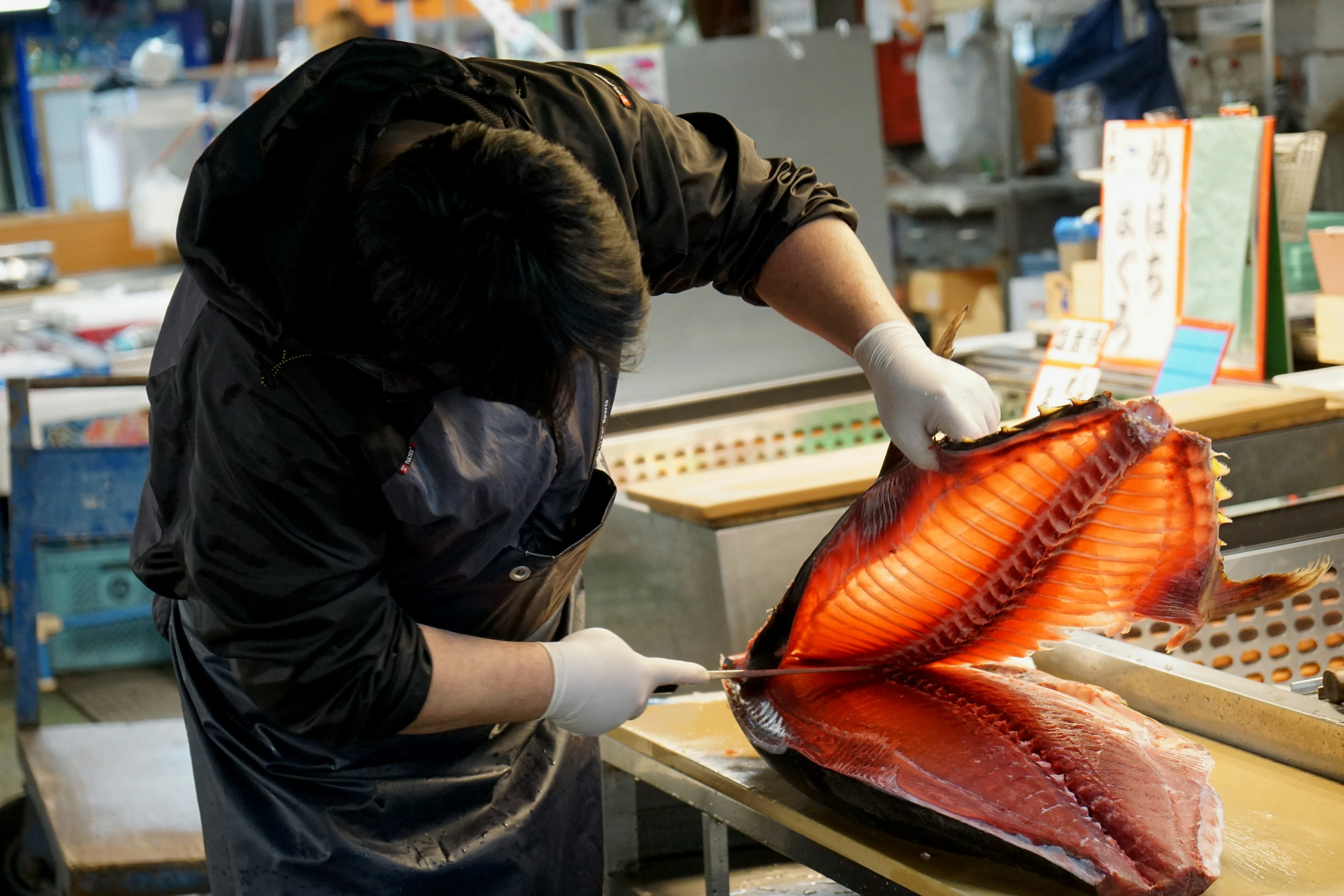 Un poissonnier, exemple typique des métiers de bouche en grande distribution, qui coupe et prépare un morceau de thon