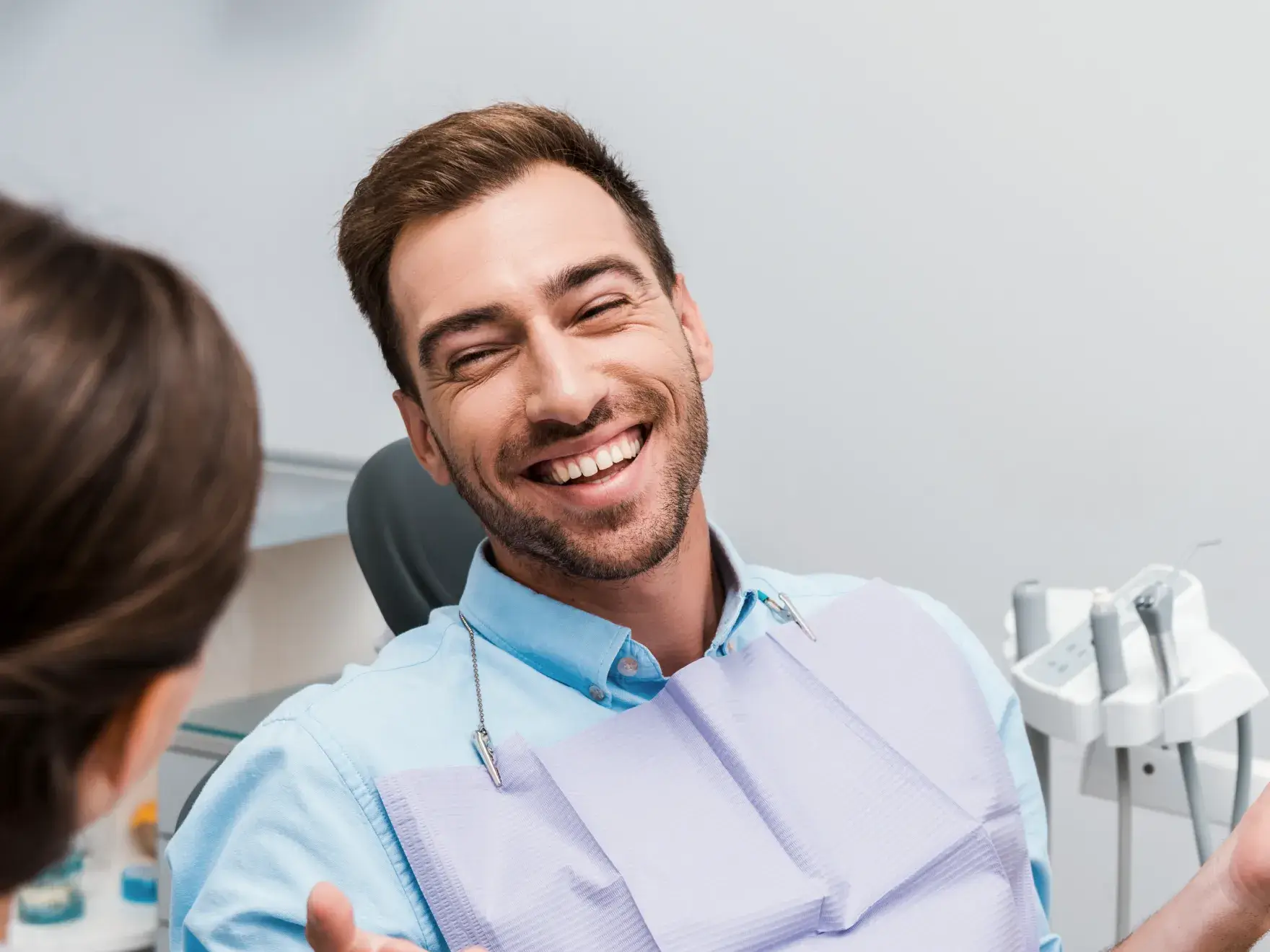 Man sitting in a dental chair, smiling widely, with a dental assistant nearby.
