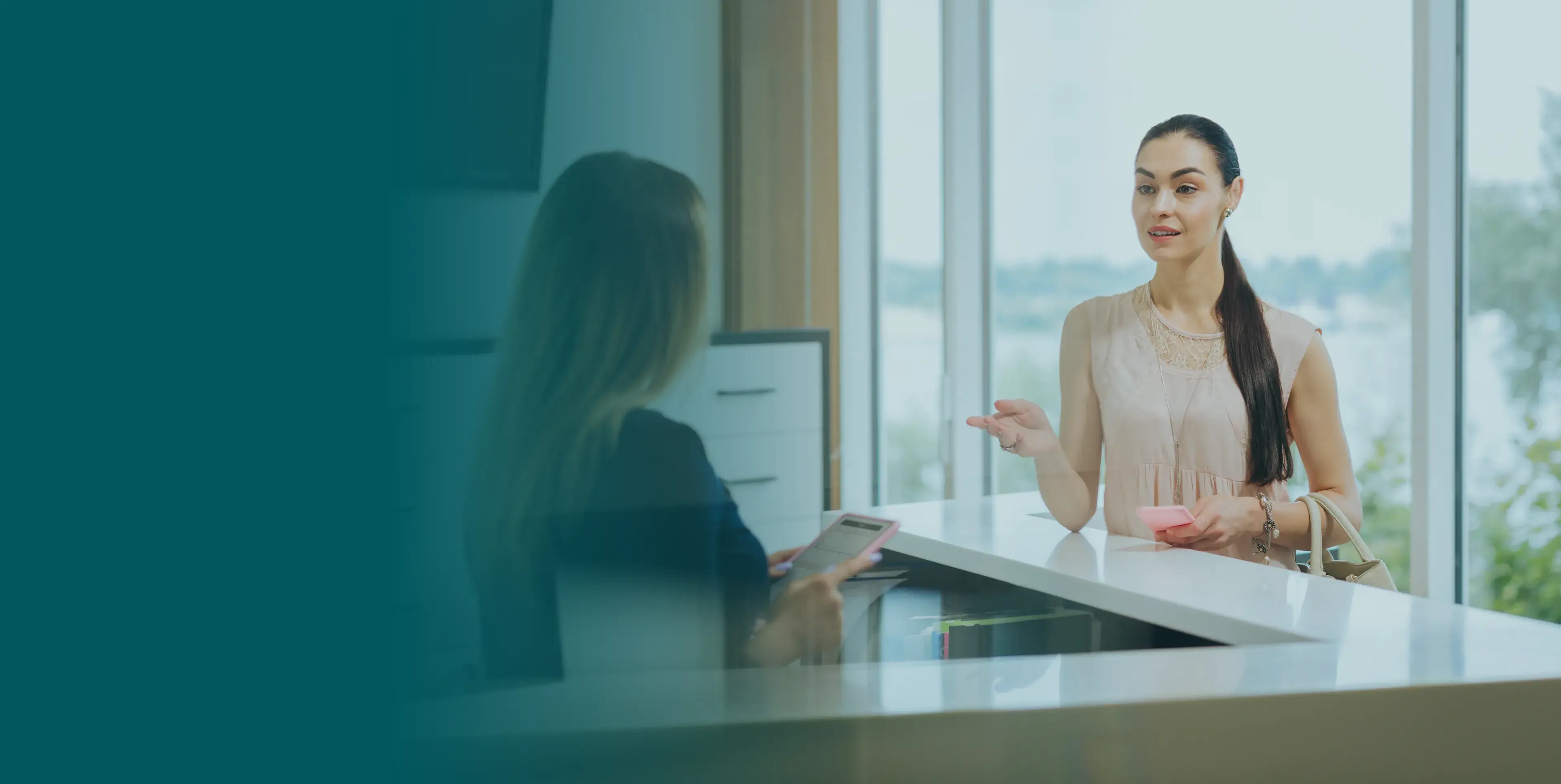 Woman talking to a receptionist at a desk in an office setting.