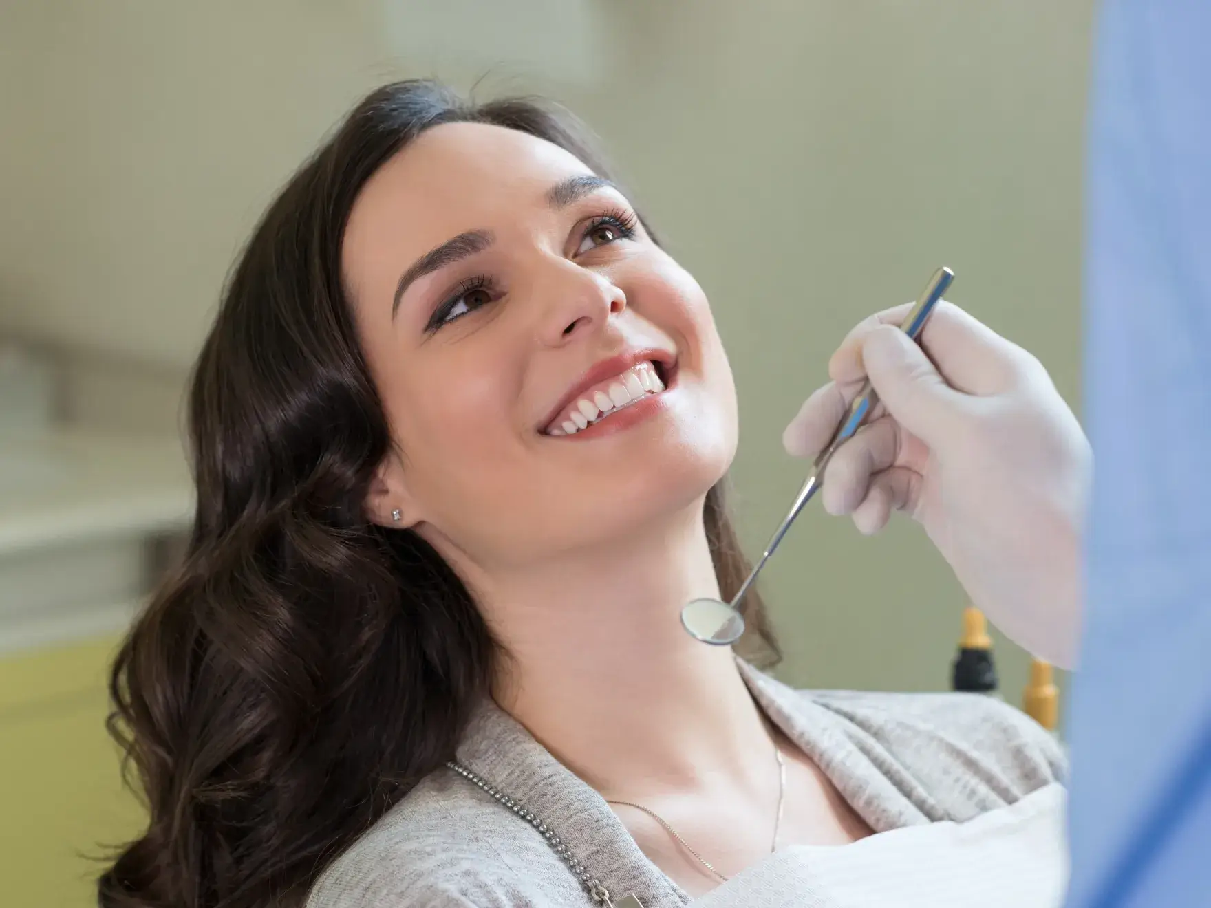 A woman smiles while a dentist holds a dental mirror near her mouth.