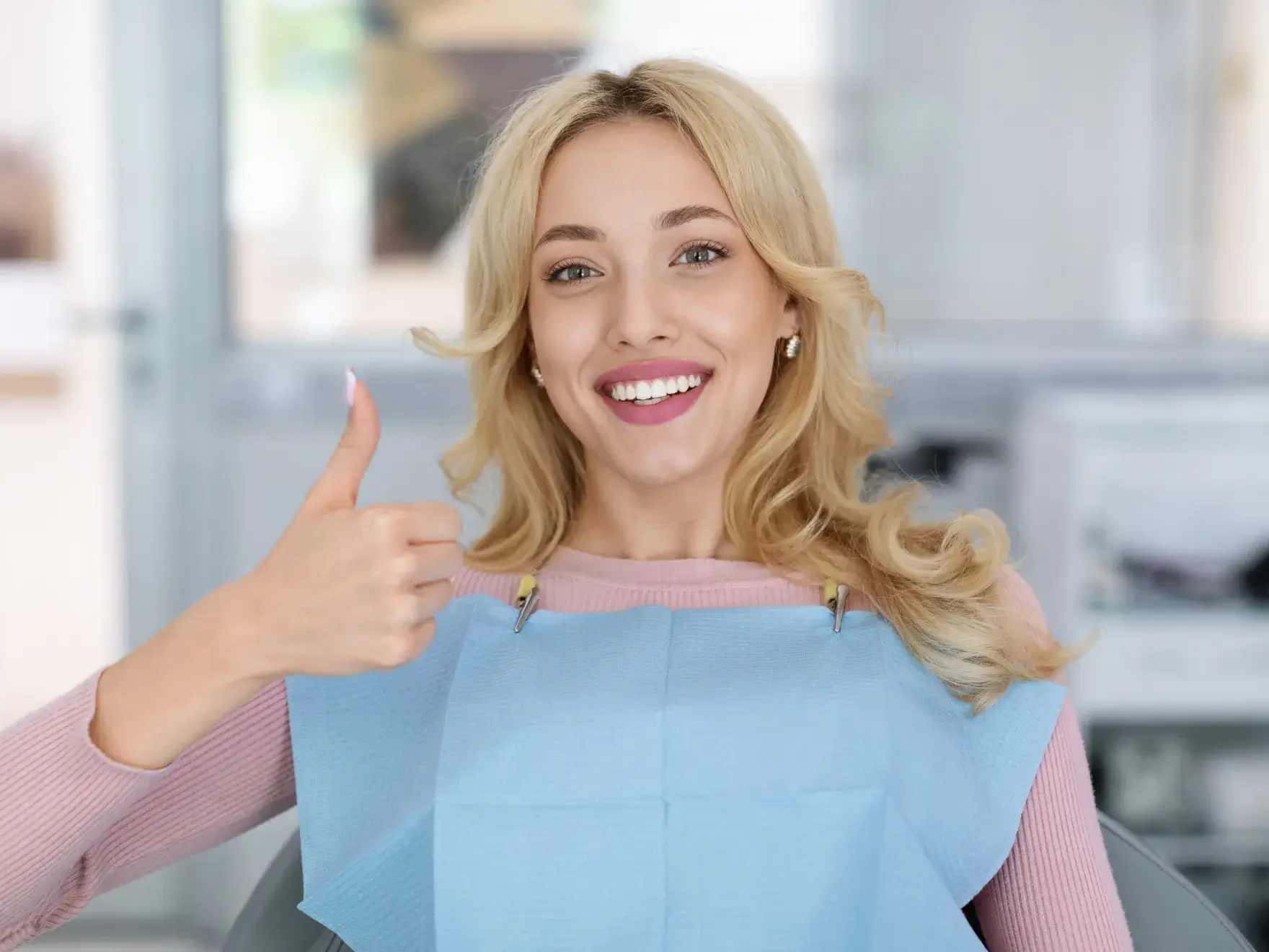 A woman sitting in a dental office giving a thumbs-up, wearing a dental bib.