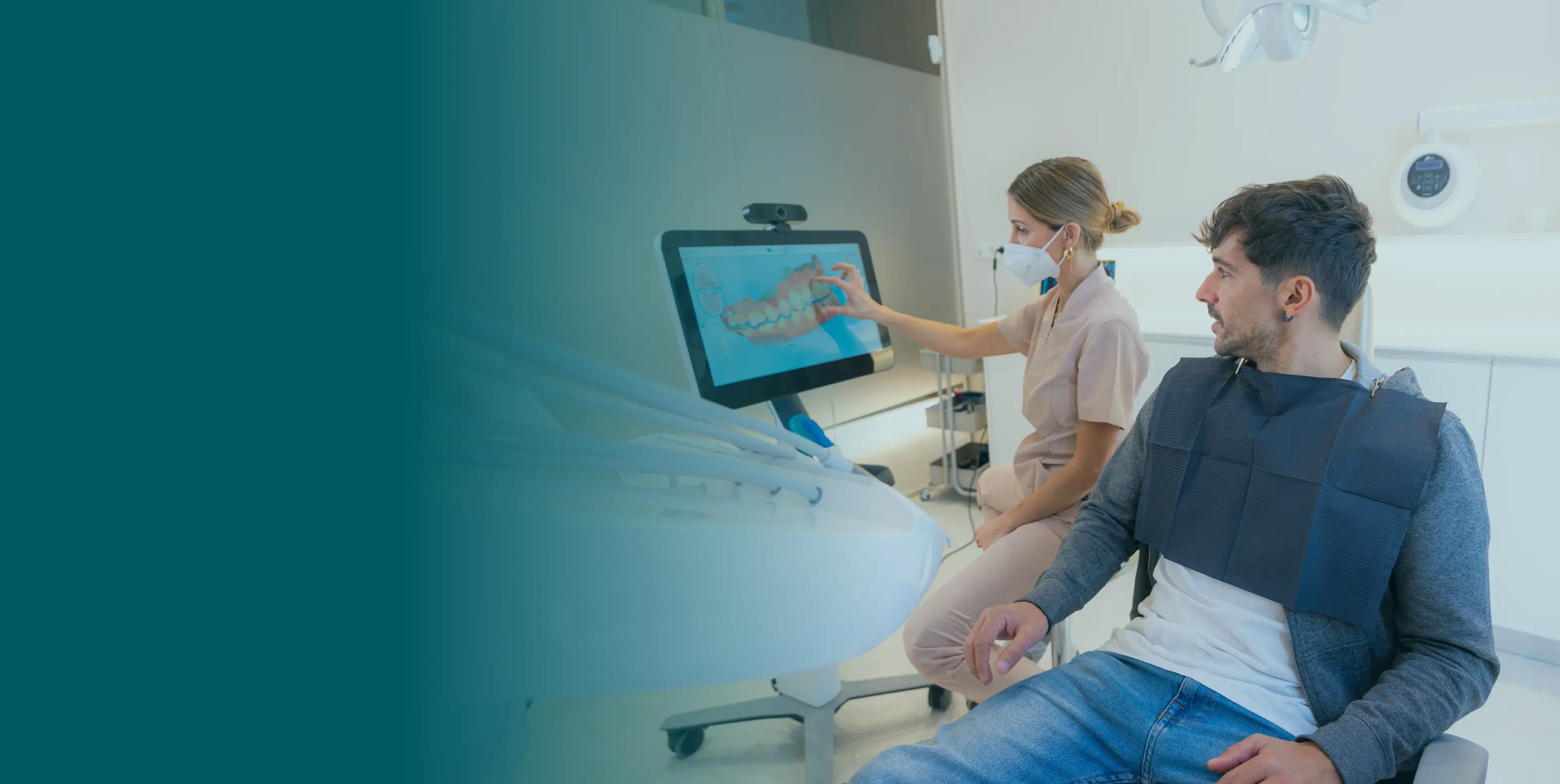 A dentist shows a patient an image of teeth on a monitor in a dental office.