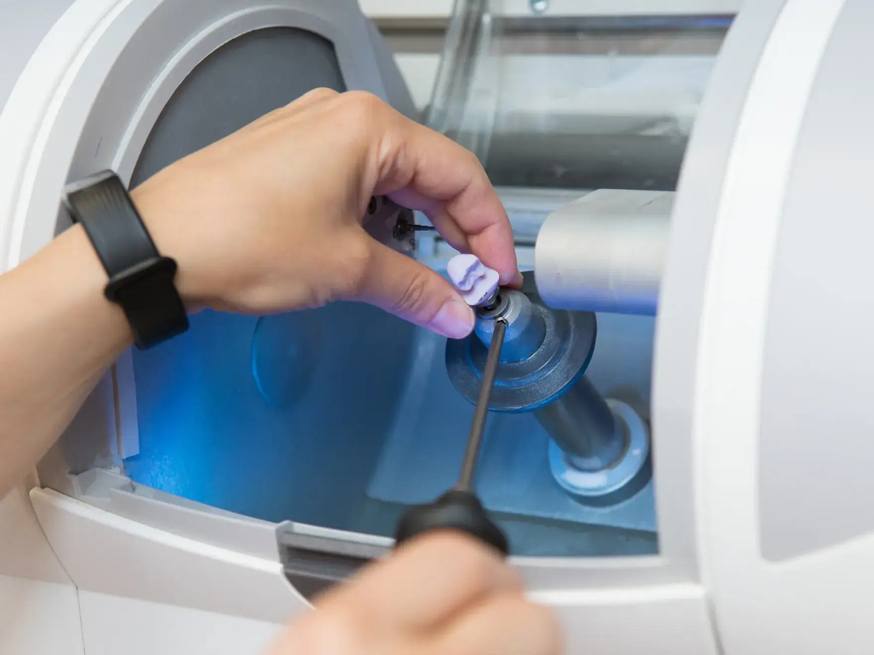 A person adjusts a dental milling machine with a tool, preparing it for use.