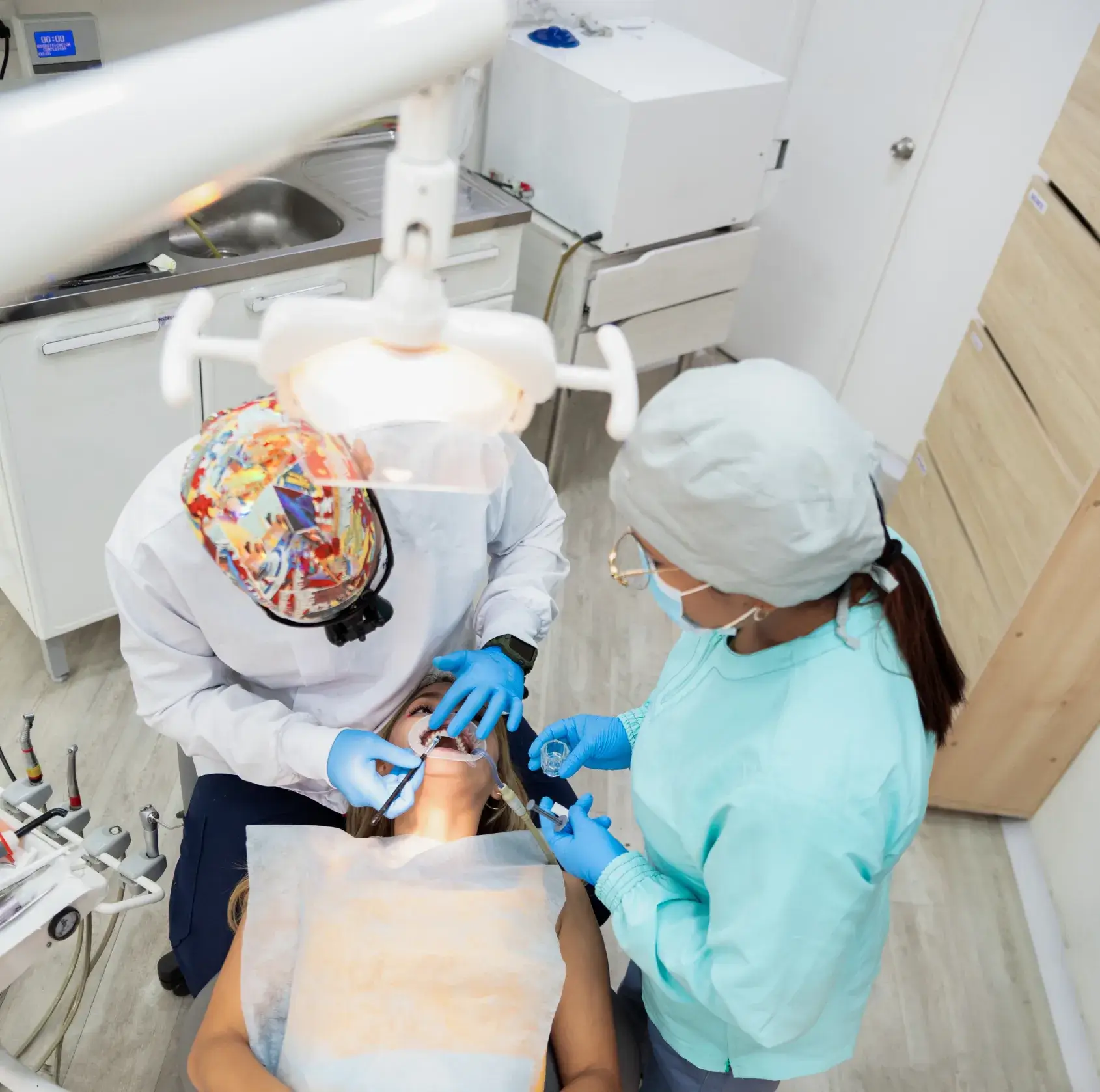 A dentist and assistant perform a dental procedure on a patient lying in a dental chair.