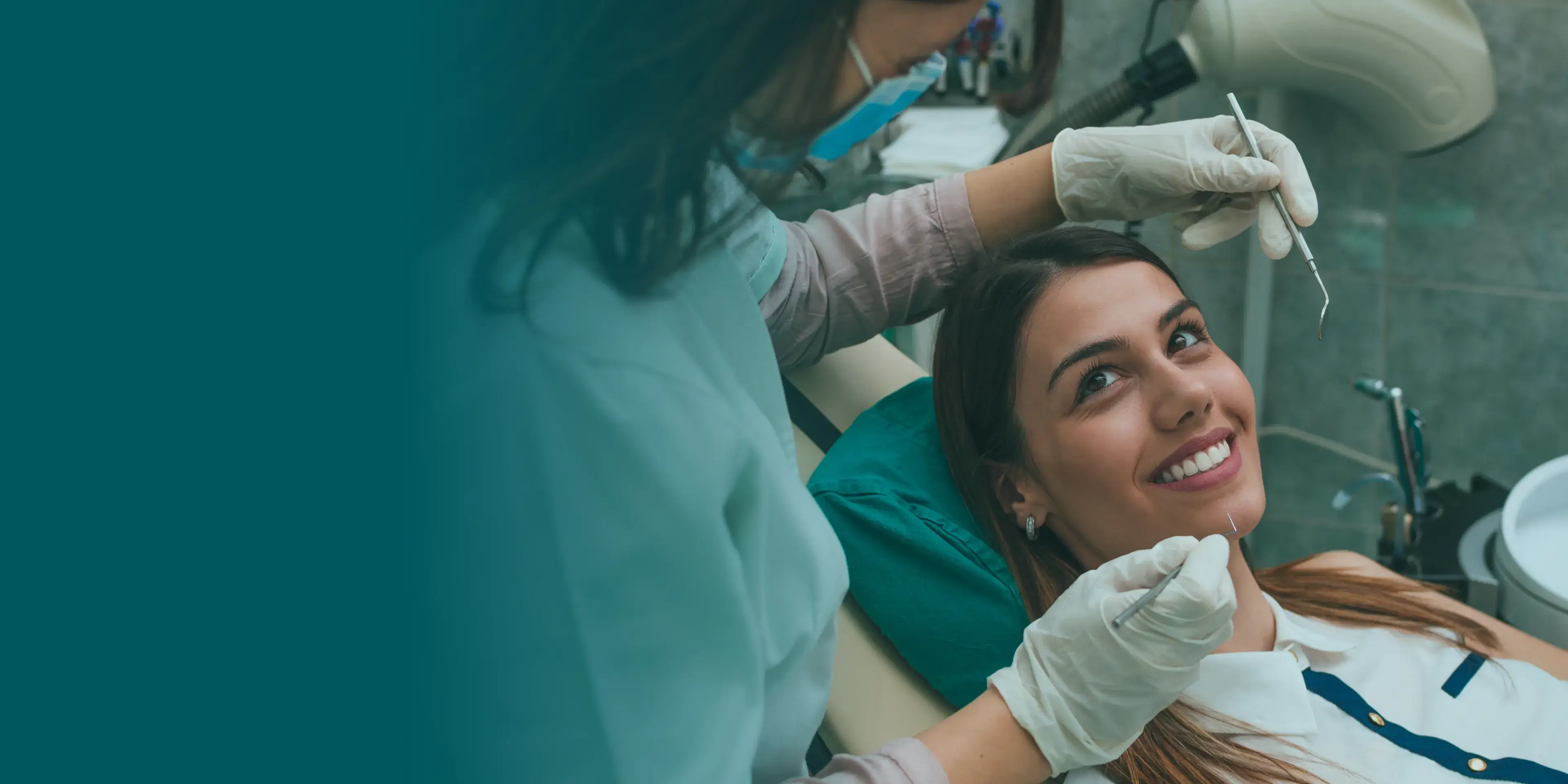A dentist examines a smiling patient's teeth with dental tools.