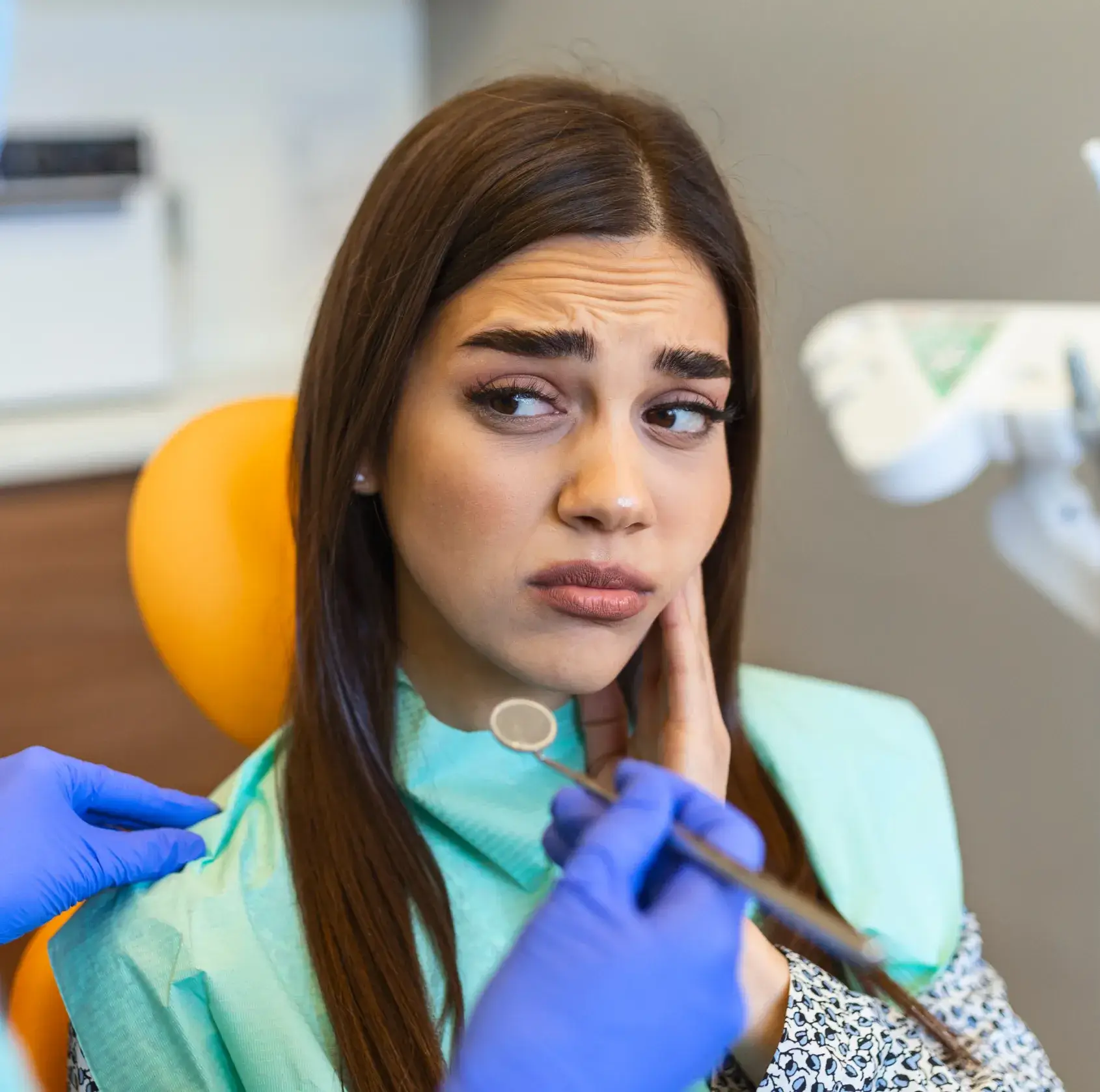 A woman in a dental chair looks concerned while a dentist holds tools near her face.