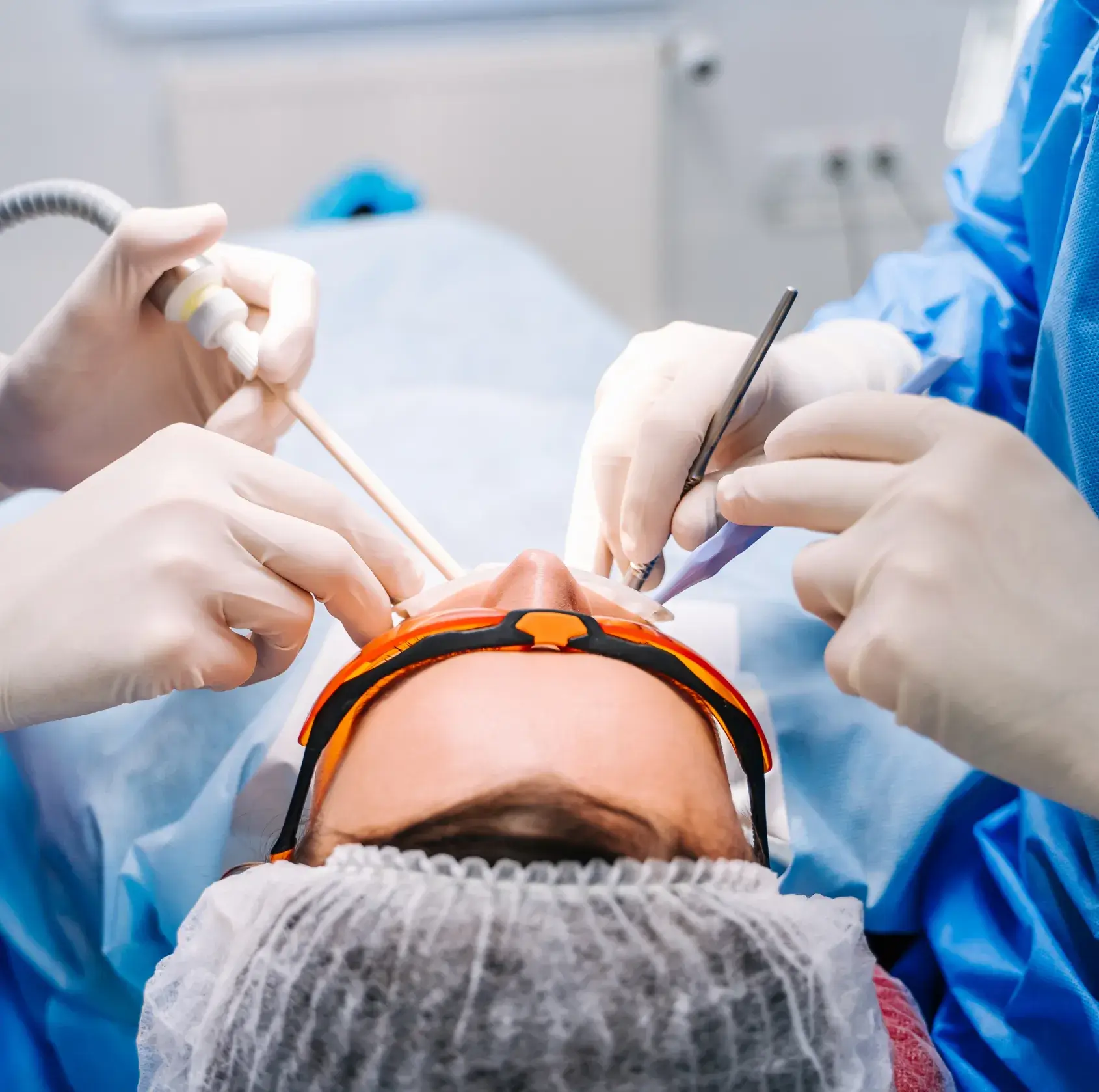 Dentists work together on a patient, wearing protective gear and using dental instruments.