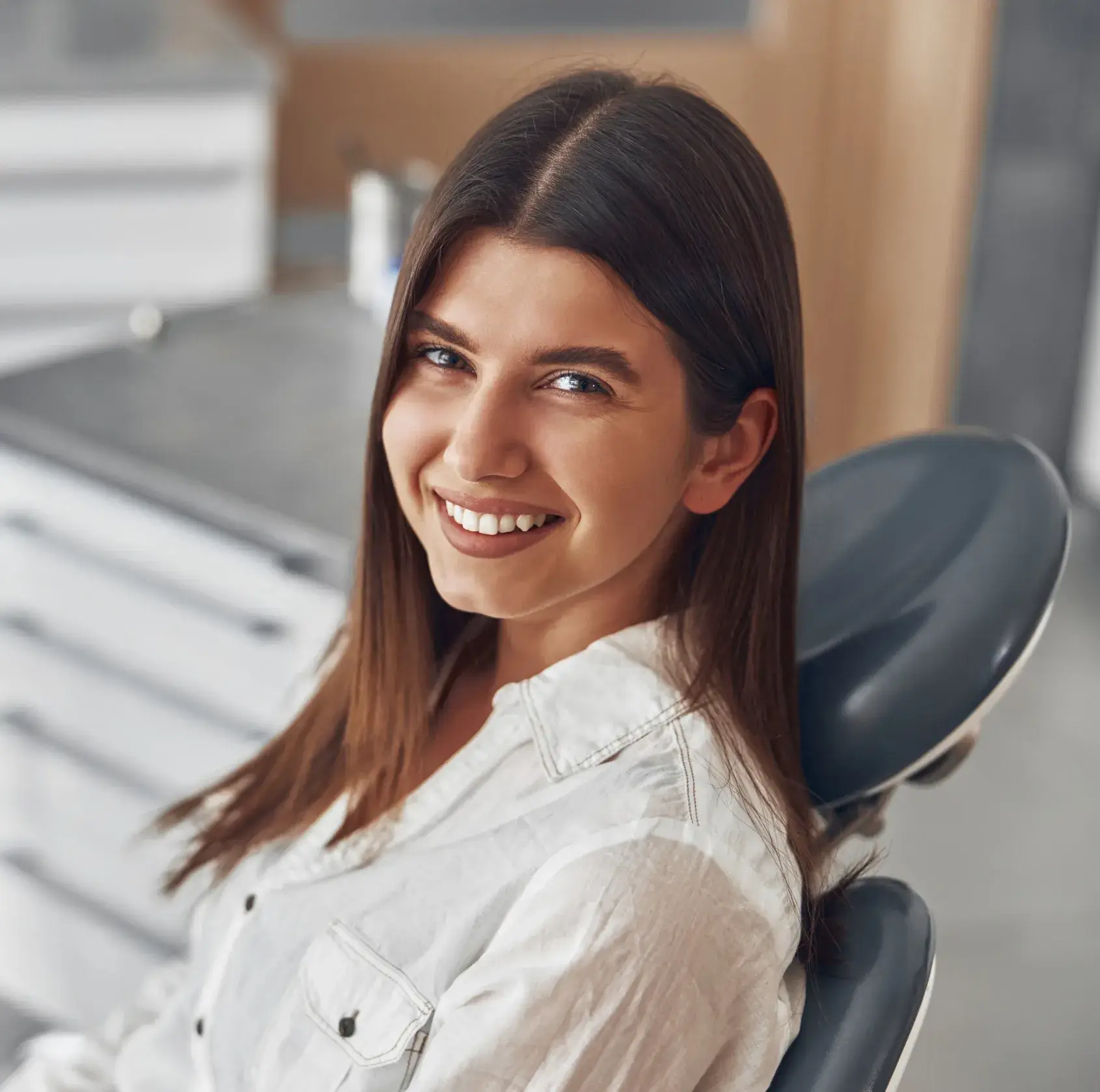 A woman sitting in a dental chair, smiling brightly at the camera.