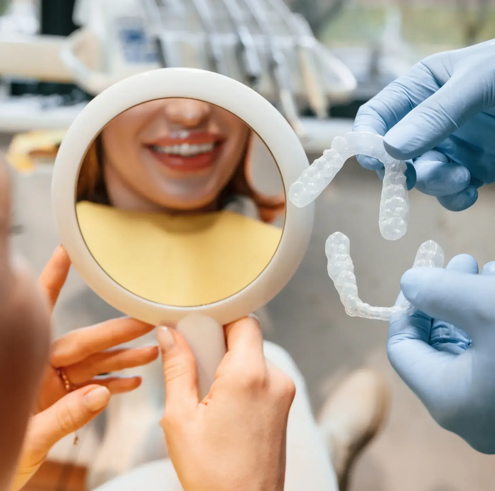 Person holding a mirror is shown clear aligners by a dentist wearing blue gloves.