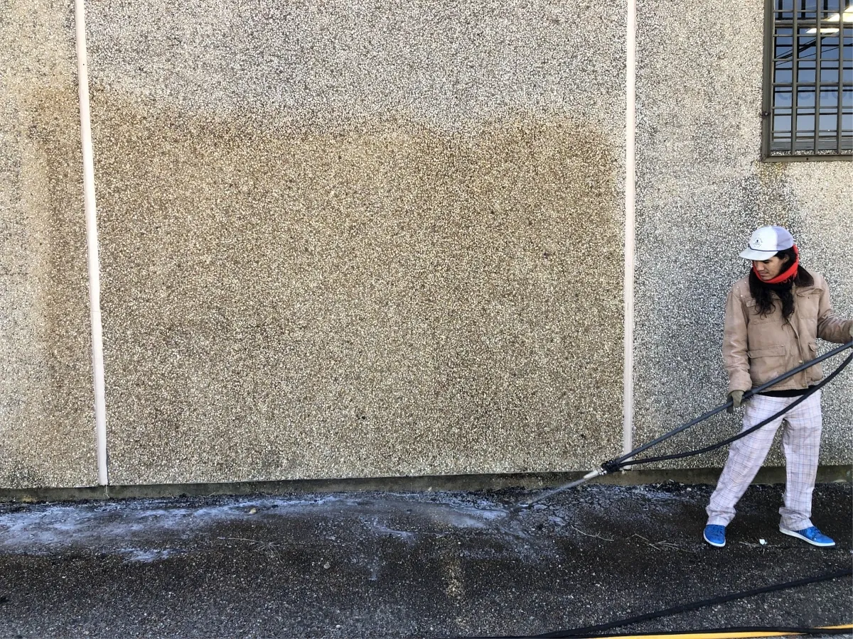 Technician pressure washing a stained concrete wall