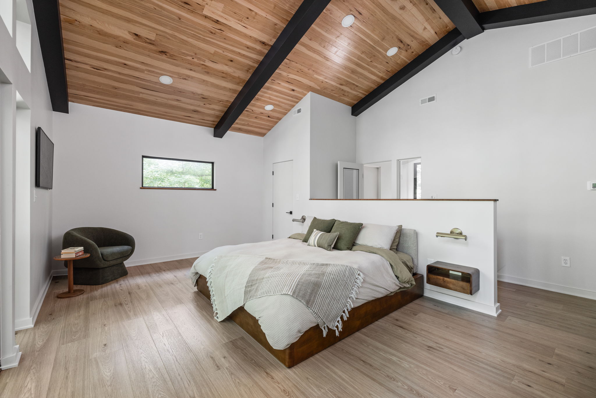 Bright primary bedroom with corner fireplace and seating area – Spacious bedroom remodel in a 1970s home addition by Emergent Construction.
