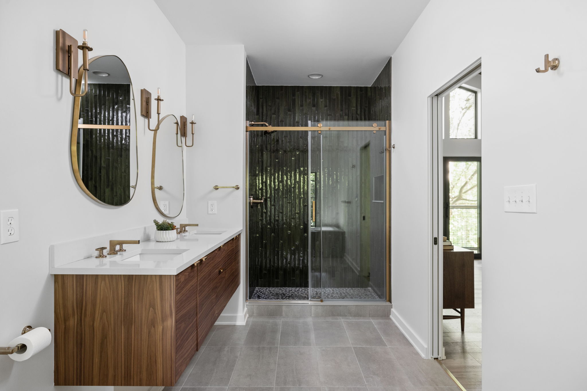 Double vanity bathroom with gold fixtures and glass shower – Luxury bathroom remodel in primary suite by Emergent Construction.