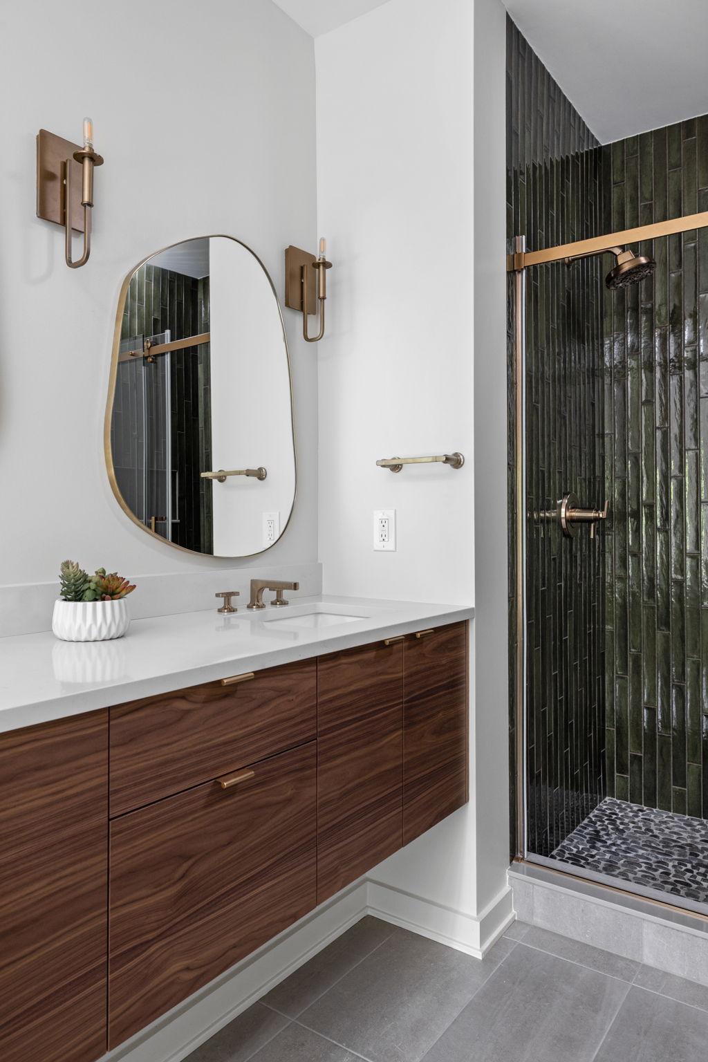 Modern bathroom with wood vanity and glass shower – Primary suite bathroom remodel by Emergent Construction featuring double vanity and gold accents.