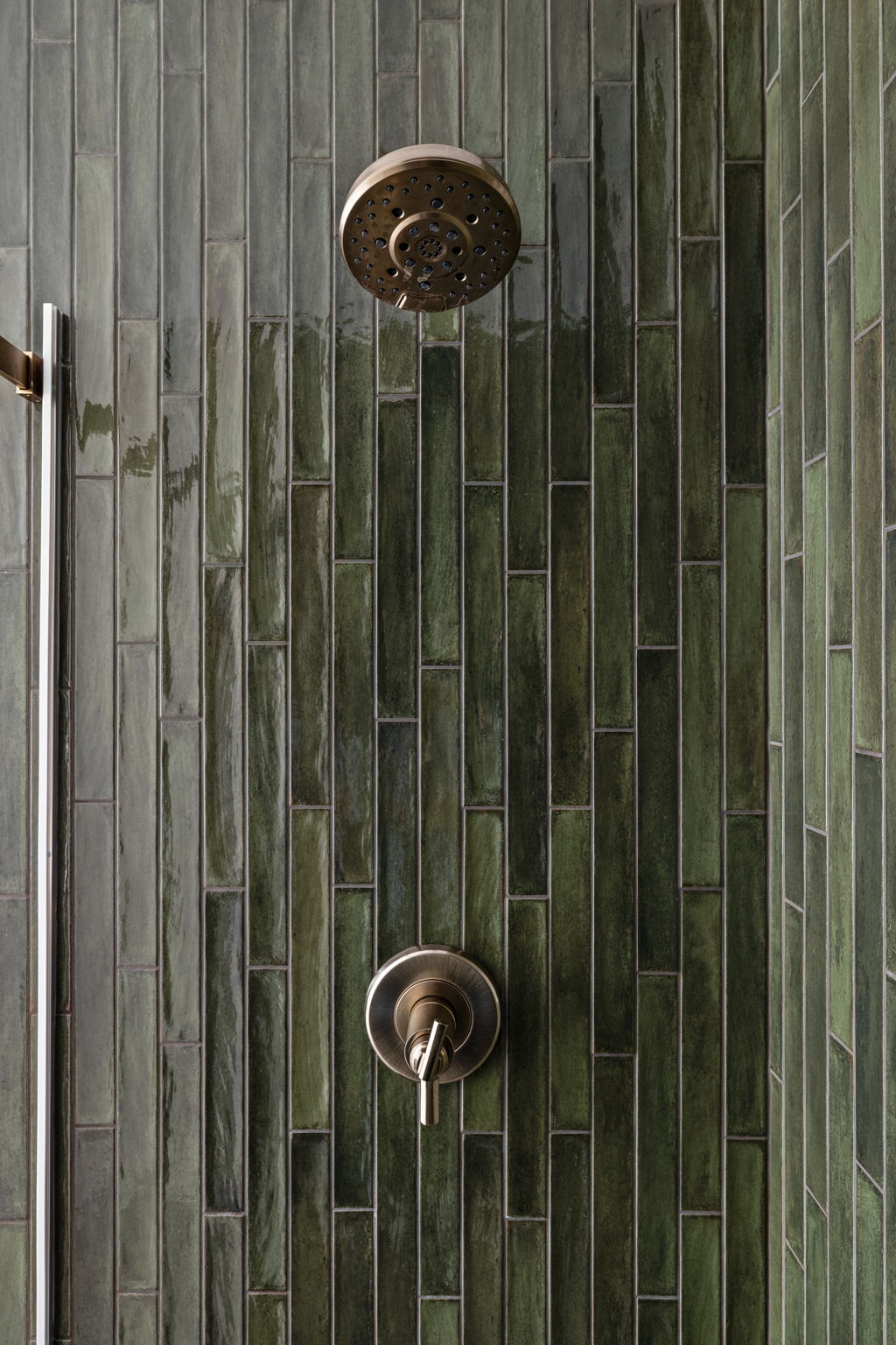Detail of vertical green tile shower with brass fixtures – Custom bathroom design in home addition by Emergent Construction.