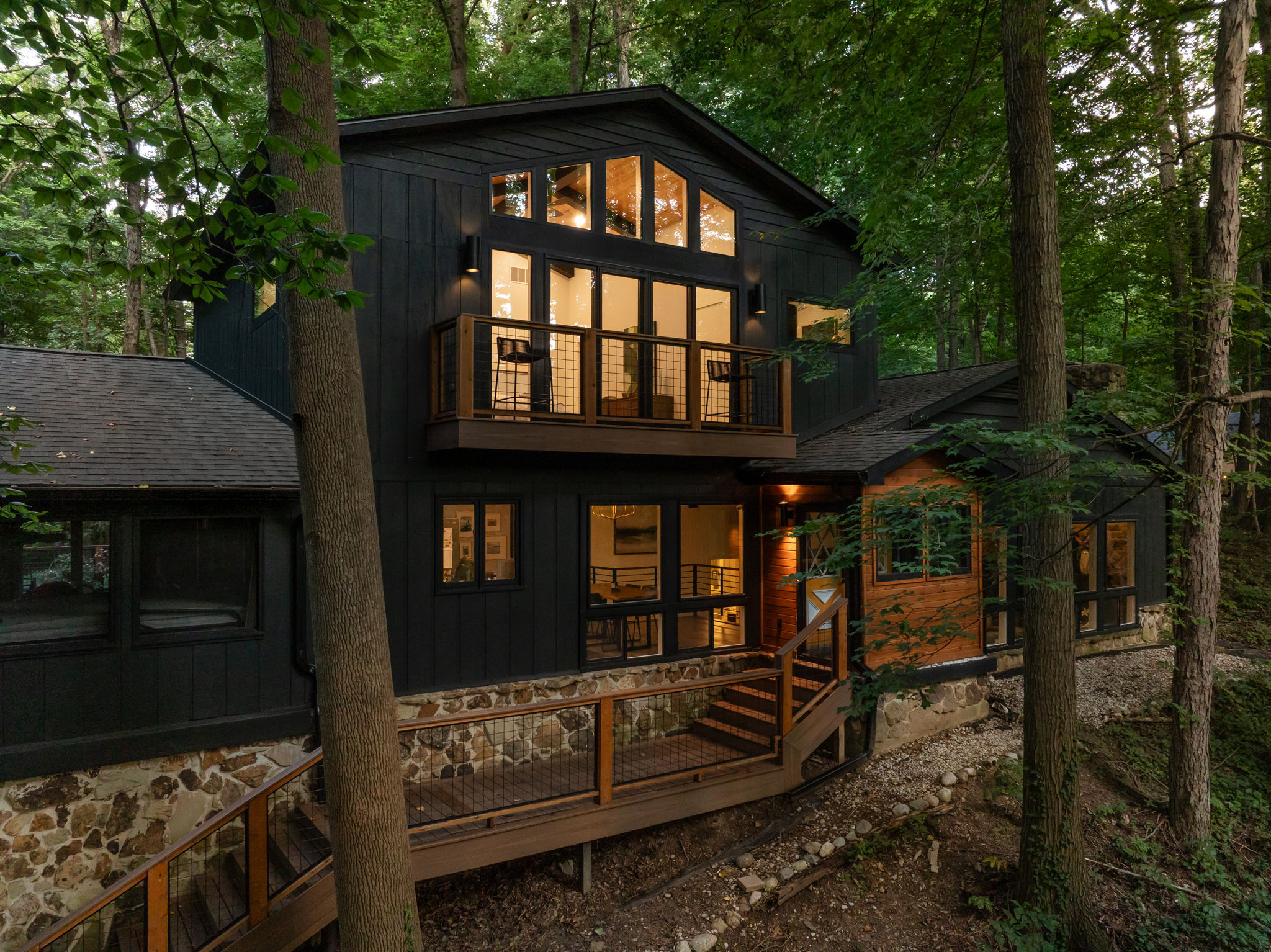Evening view of illuminated home addition with stone base – Modern exterior renovation by Emergent Construction.