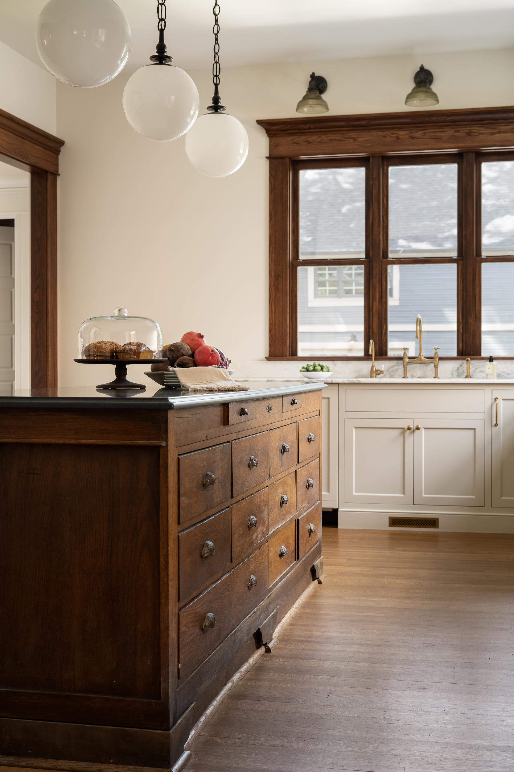 Historic kitchen renovation with a dark wood island, cream perimeter cabinets, and vintage-inspired lighting.