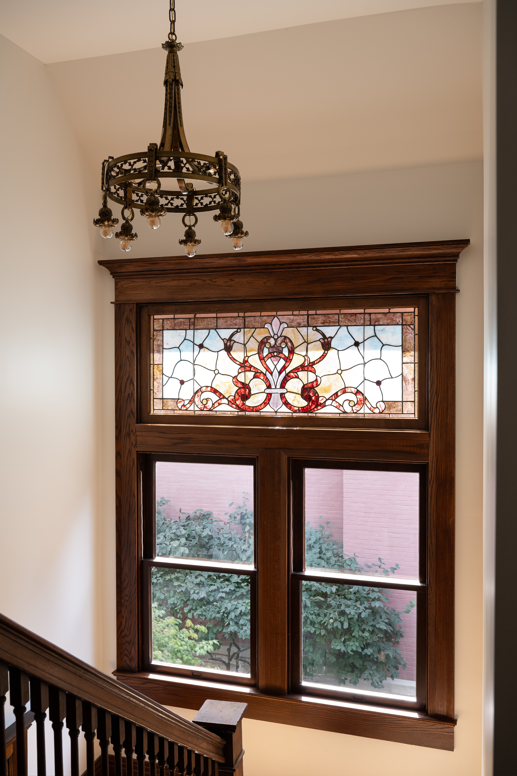 Original Victorian staircase window featuring decorative stained glass, rich wood trim, and hanging light fixture.