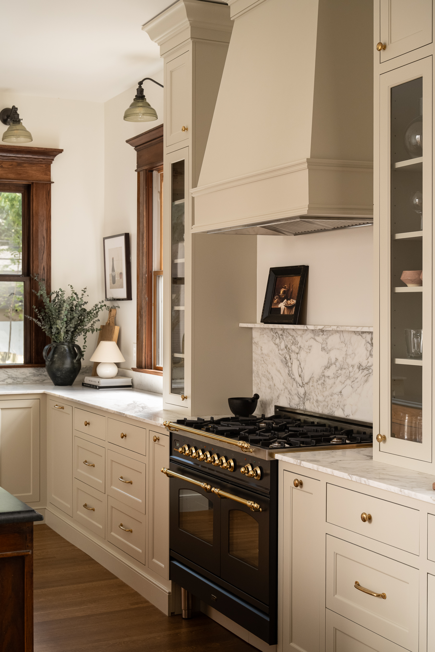 Renovated Victorian kitchen featuring cream cabinetry, a statement range hood, and dark stove.
