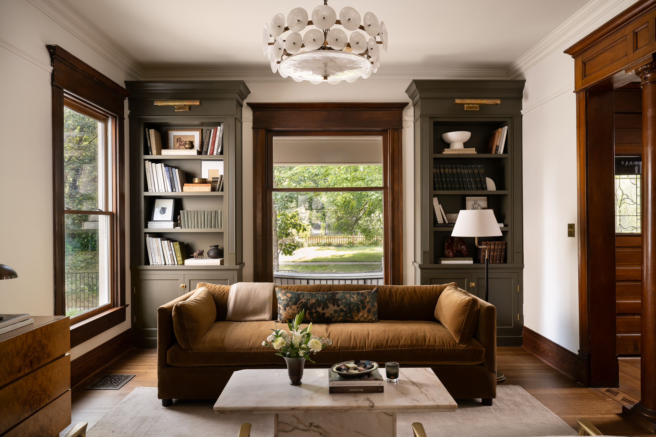 Victorian living room with original dark wood trim, built-in shelving, a large window, and warm neutral furnishings.