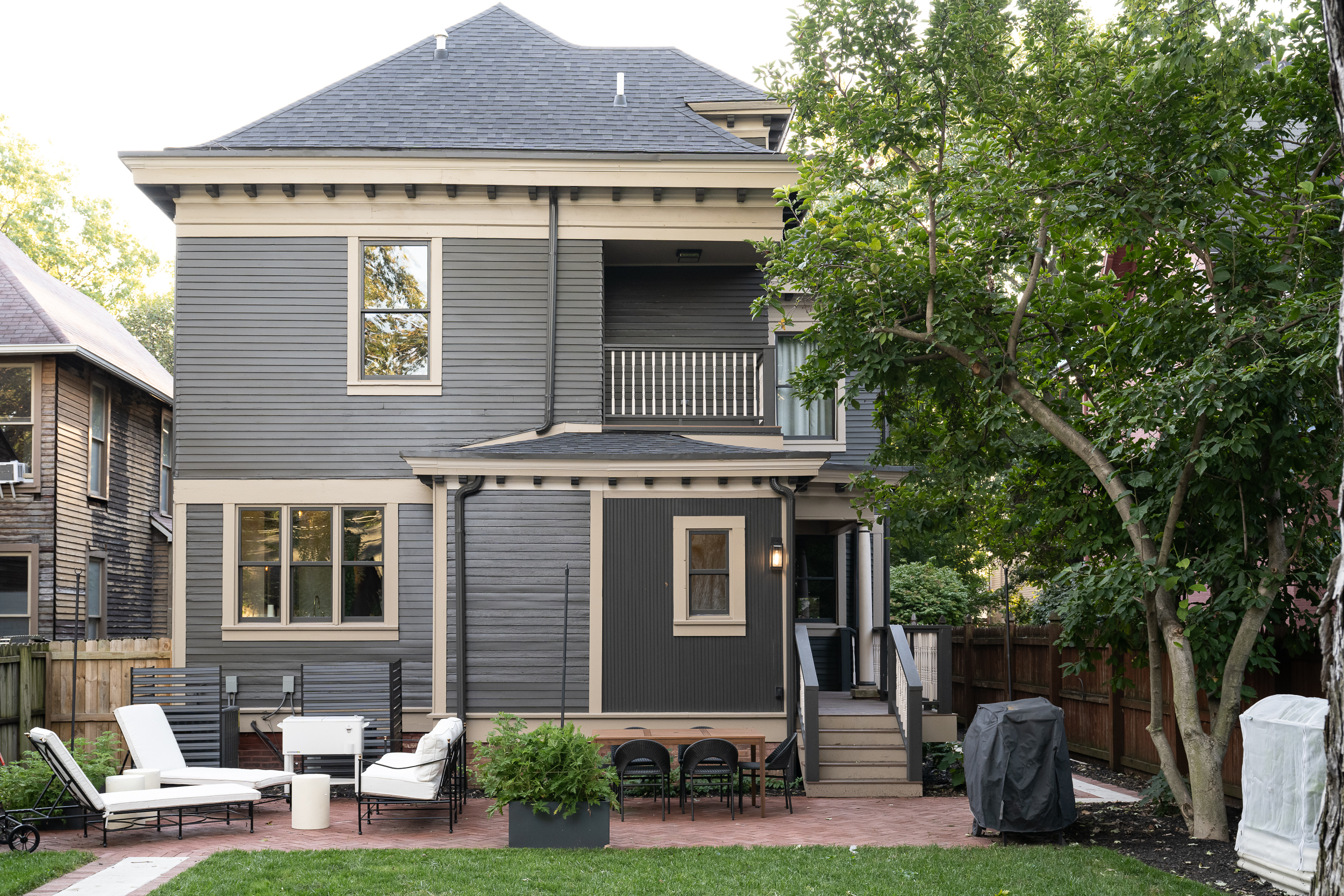 Rear exterior of restored Victorian home with gray siding, white trim, and landscaped backyard.