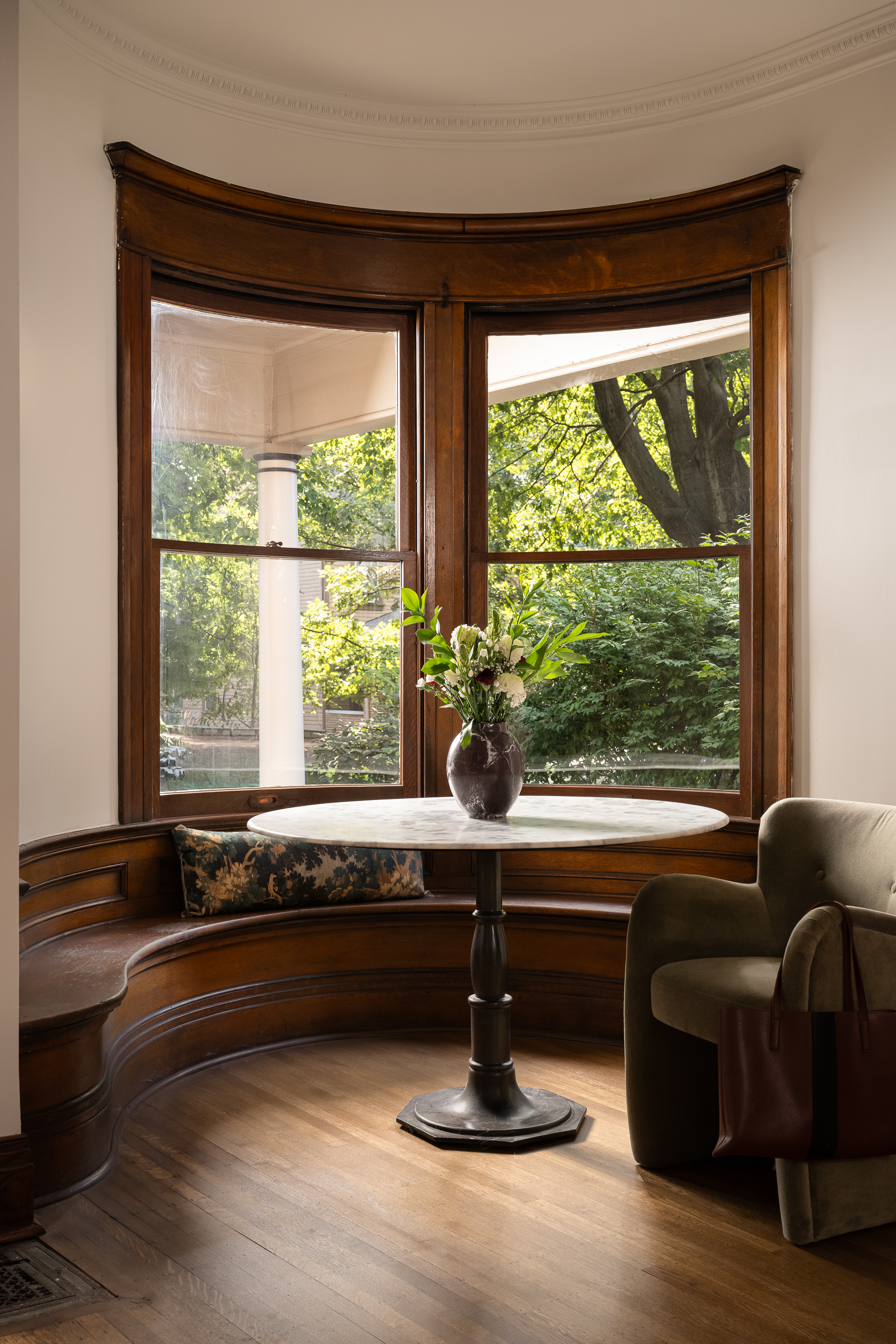 Cozy Victorian bay window seating area with rich wood trim, natural light, and a small round table.