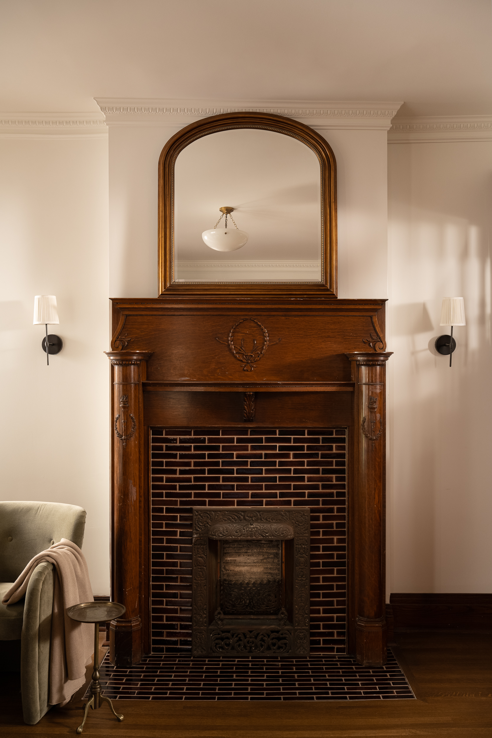 Historic fireplace with an ornate wood mantel, decorative tile surround, and arched mirror.