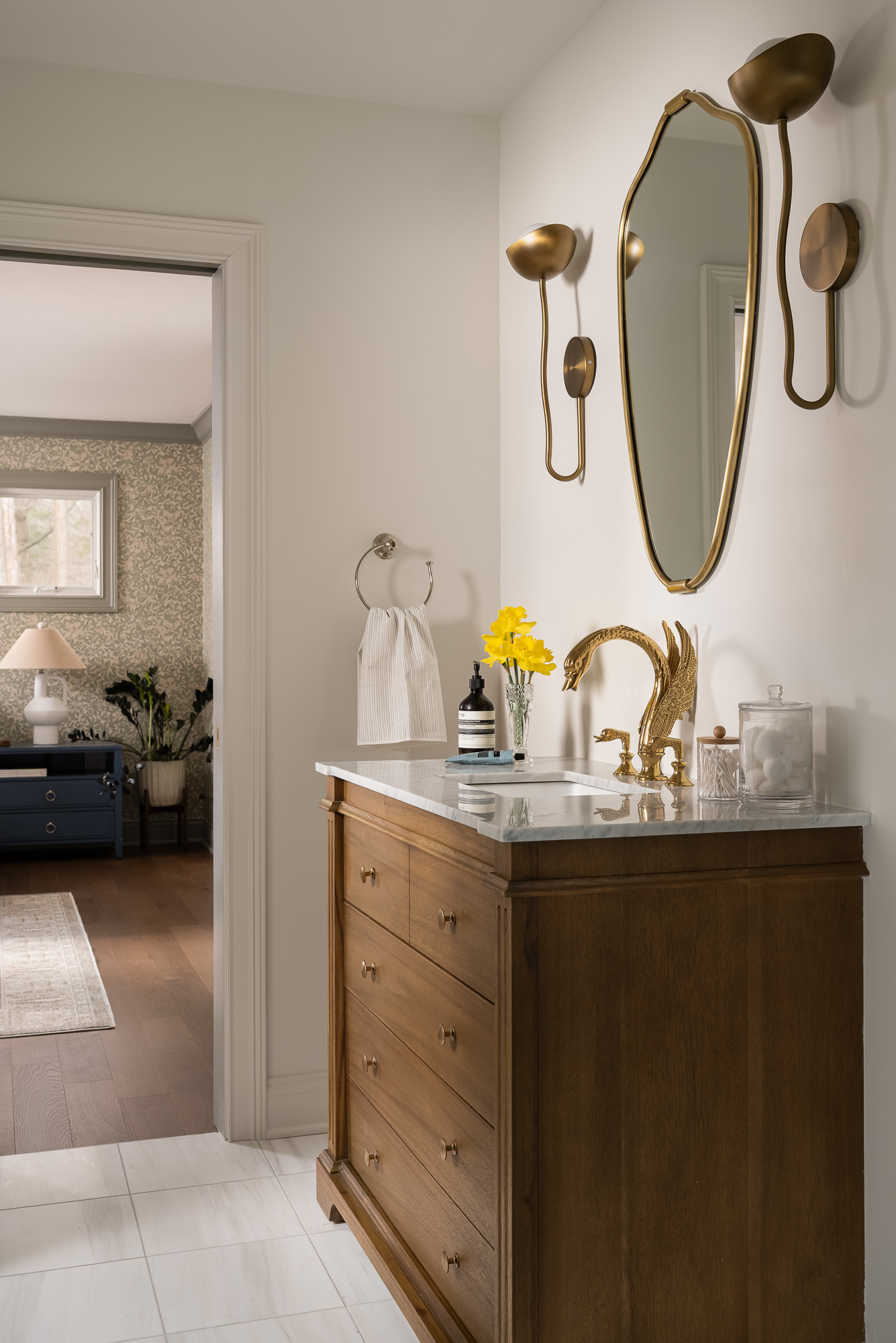Renovated bathroom featuring a natural wood vanity, white countertop, brass fixtures, and an arched mirror.