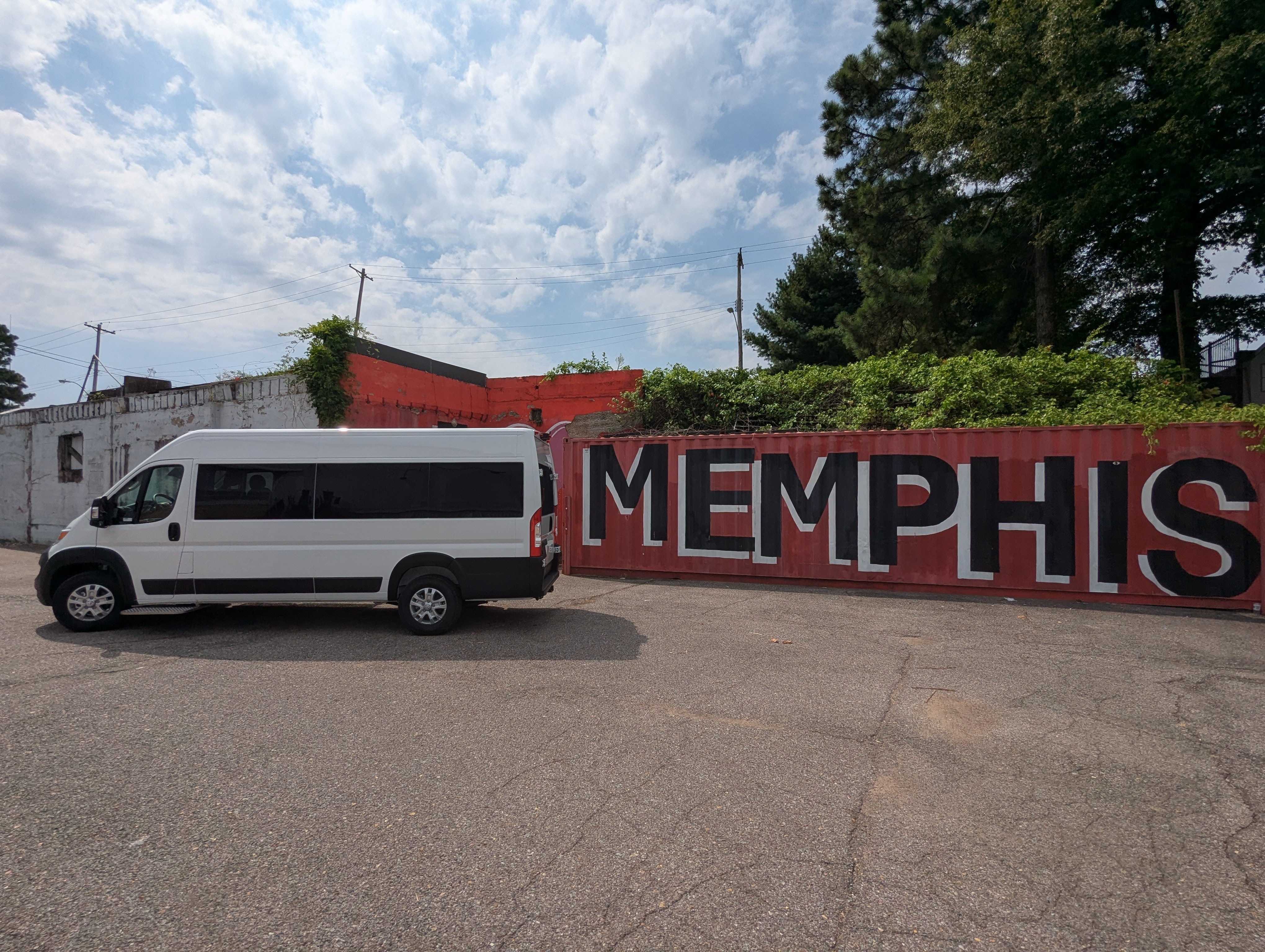White passenger van parked beside a red container with large black letters spelling MEMPHIS, under a partly cloudy sky.