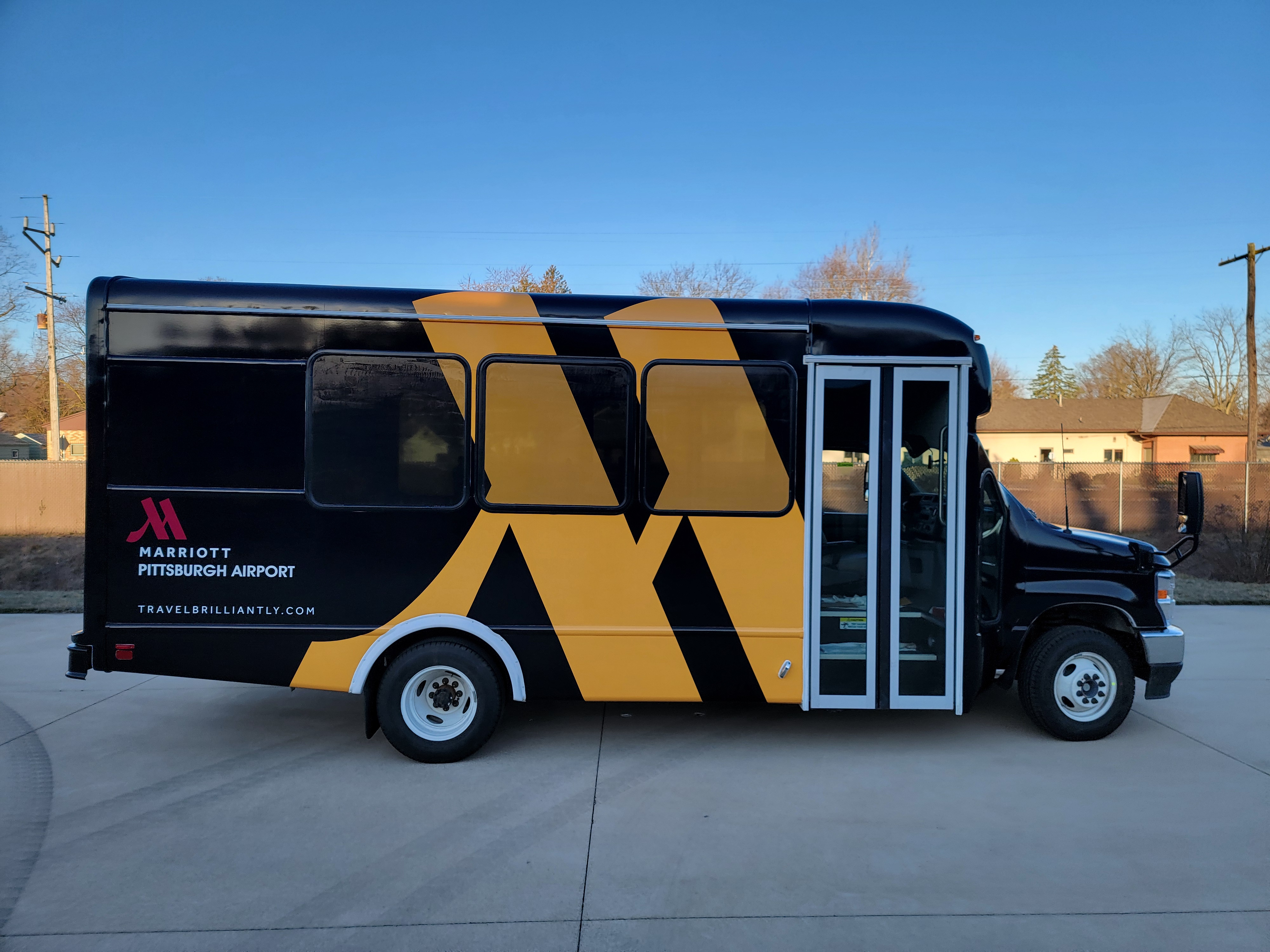Black and yellow Marriott Pittsburgh Airport shuttle bus parked on concrete under clear blue sky.
