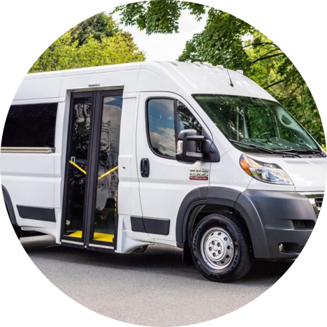 White passenger van with open sliding door parked on a road with green trees in the background.