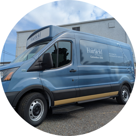 Blue Fairfield by Marriott Columbus OSU shuttle van parked outside a white building under a partly cloudy sky.