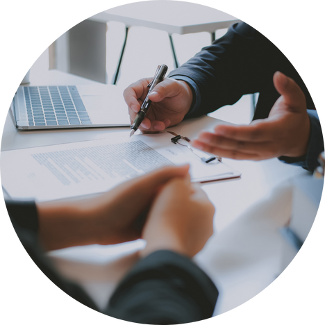 Close-up of two people discussing a document with a pen and laptop on the table in an office setting.