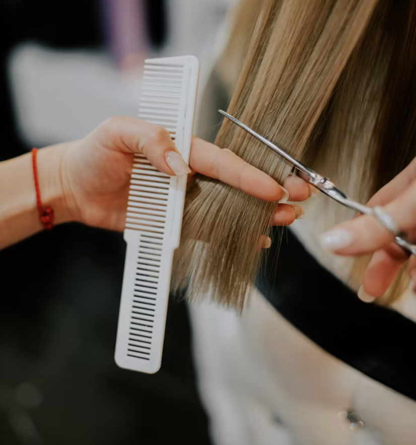 Close-up of a hairdresser cutting light brown hair using scissors and a white comb.