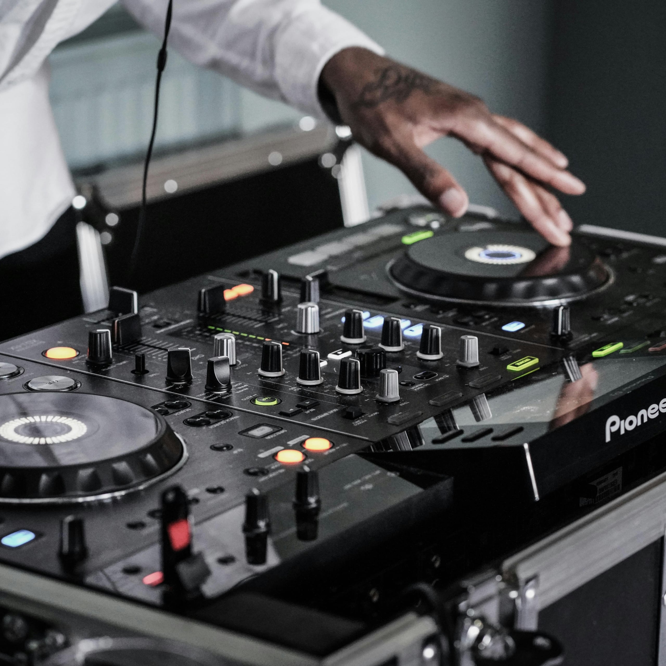 Close-up of a DJ's hand adjusting controls on a Pioneer DJ mixer with lit buttons and dials.