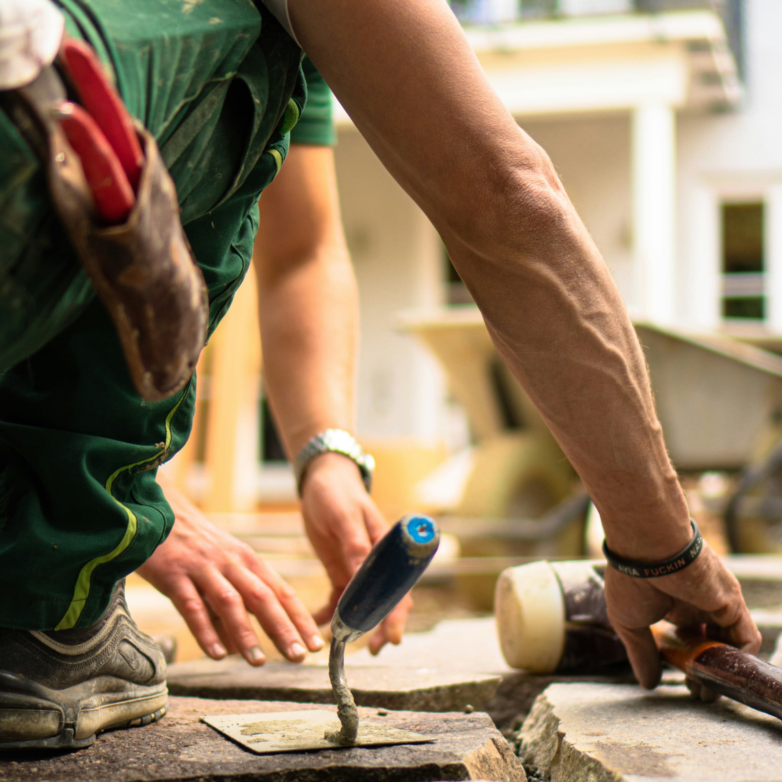Worker laying stone slabs with a trowel and mallet on a ground surface outdoors.