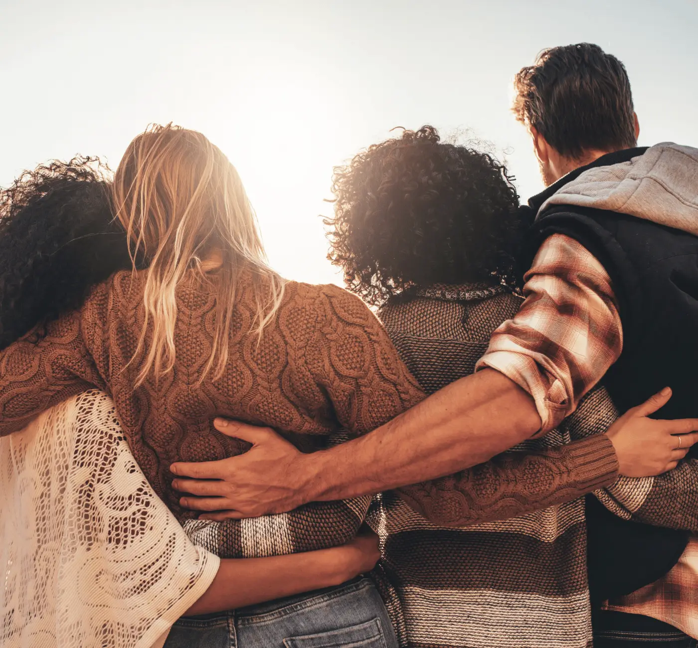 Diverse group of friends embracing at sunset, symbolizing community, support, and connection.