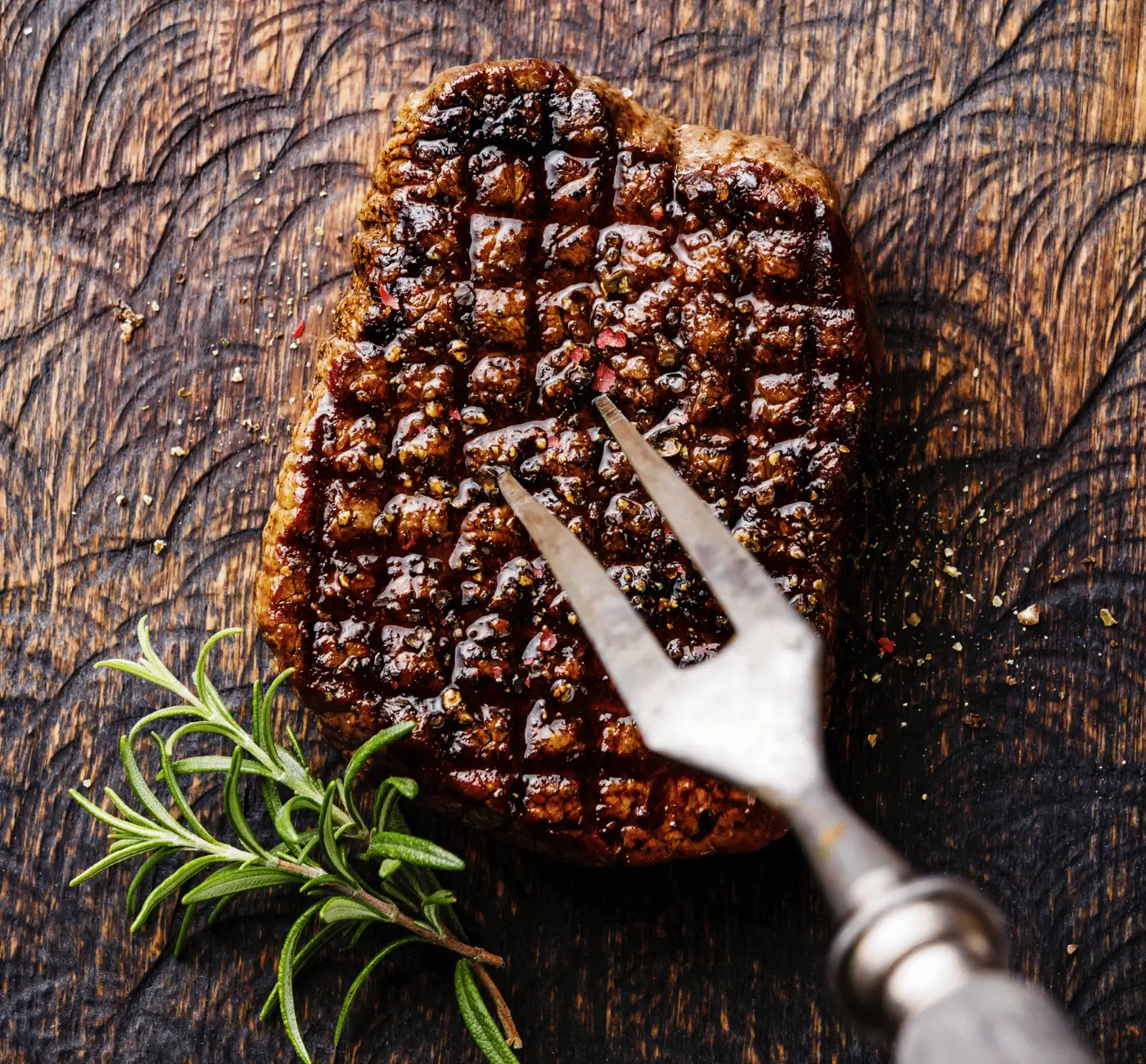 Chargrilled grass-fed steak resting on a rustic wooden board, garnished with fresh rosemary.