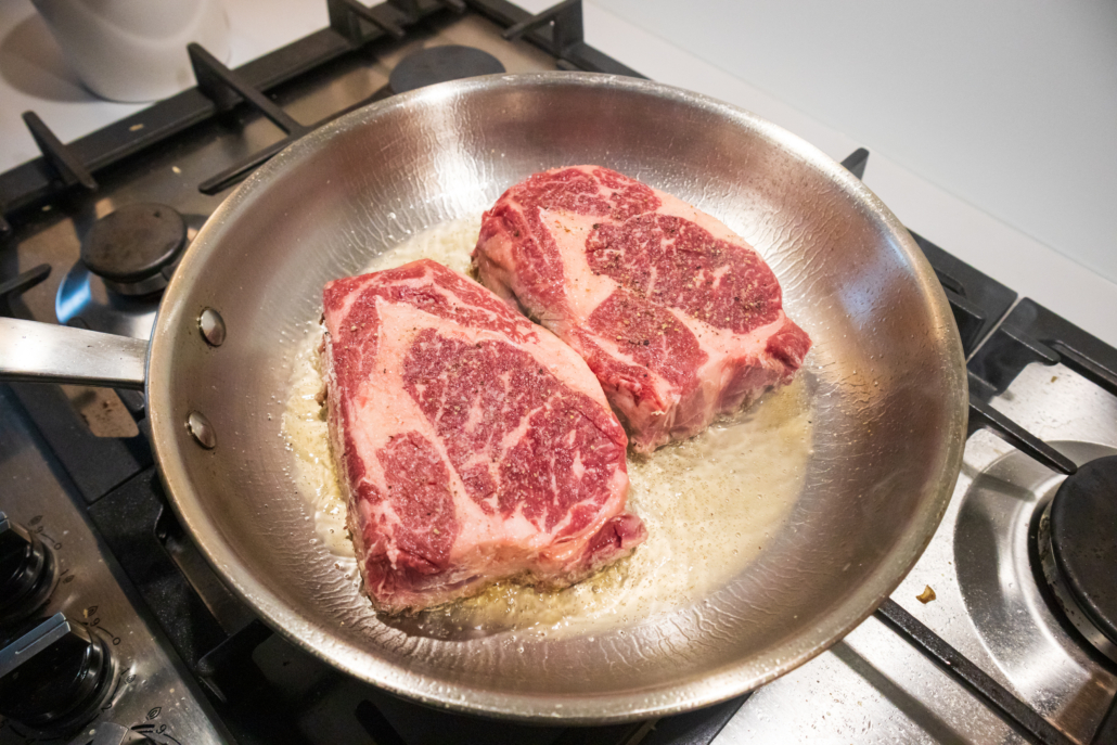 Ribeye beef steak in a stainless steel pan with butter.