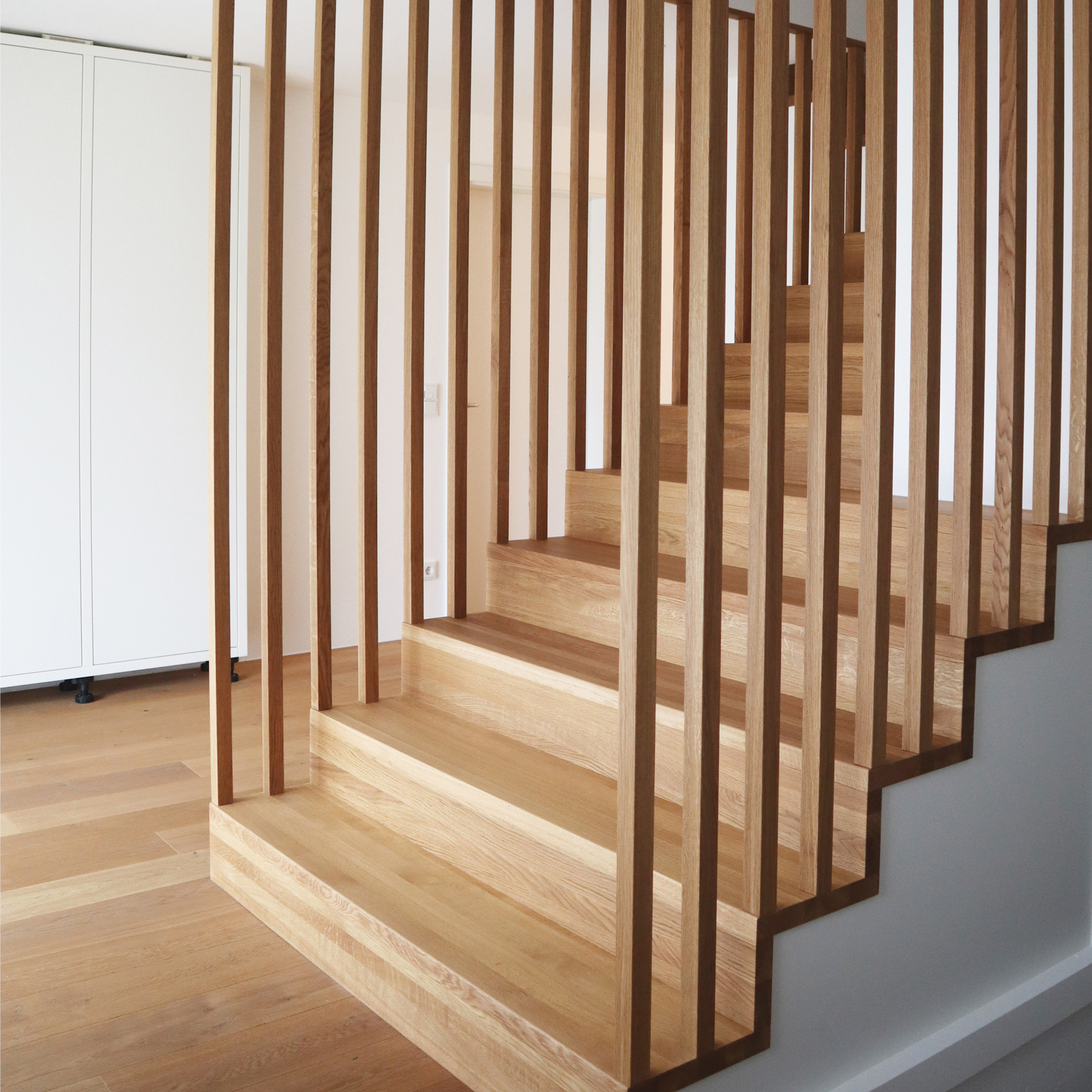 Wooden staircase with vertical slat railing in a bright modern interior.