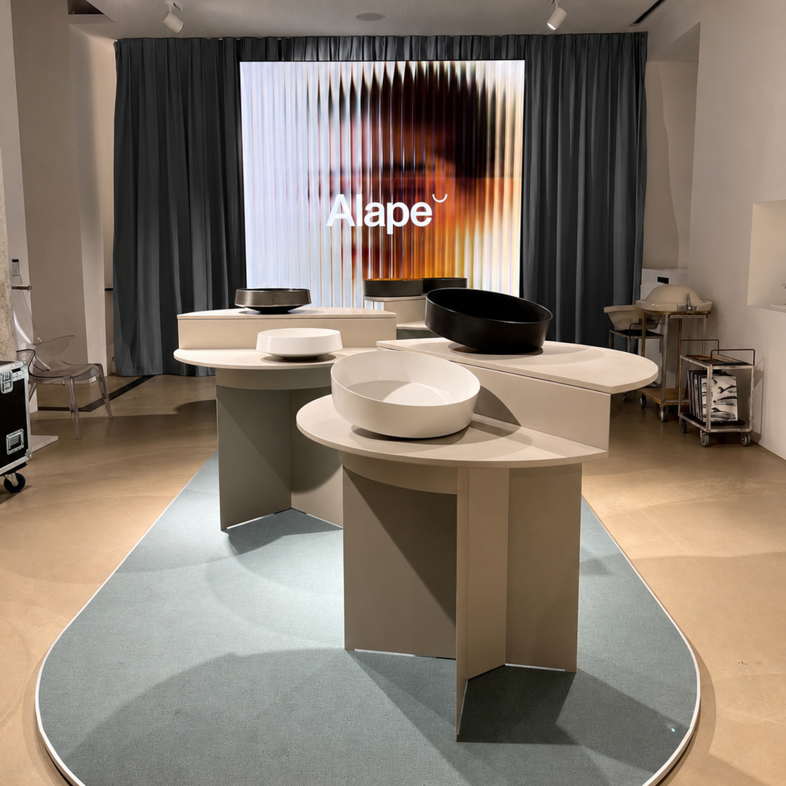 Modern showroom with white and black designer sinks displayed on curved beige tables on a gray carpet.