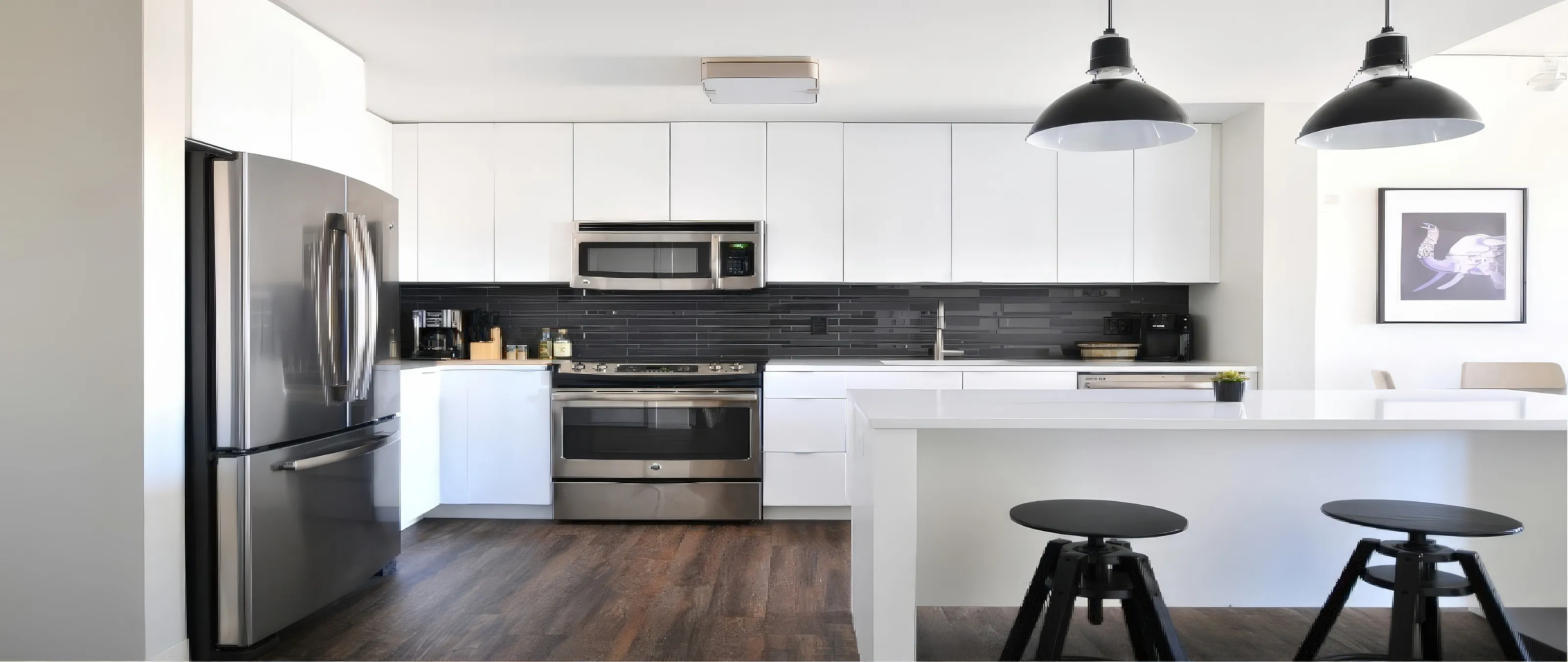 A modern kitchen with white cabinets, a stainless steel fridge, oven, and microwave. A black backsplash contrasts with white countertops. Hanging black pendant lights illuminate a breakfast bar with two black stools. A framed picture adorns the white wall.