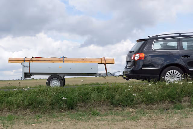 Car backing up a small trailer with some wood strapped on-top