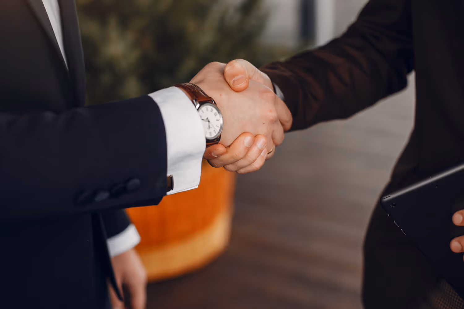 Two businesspeople in suits shaking hands in a professional setting.