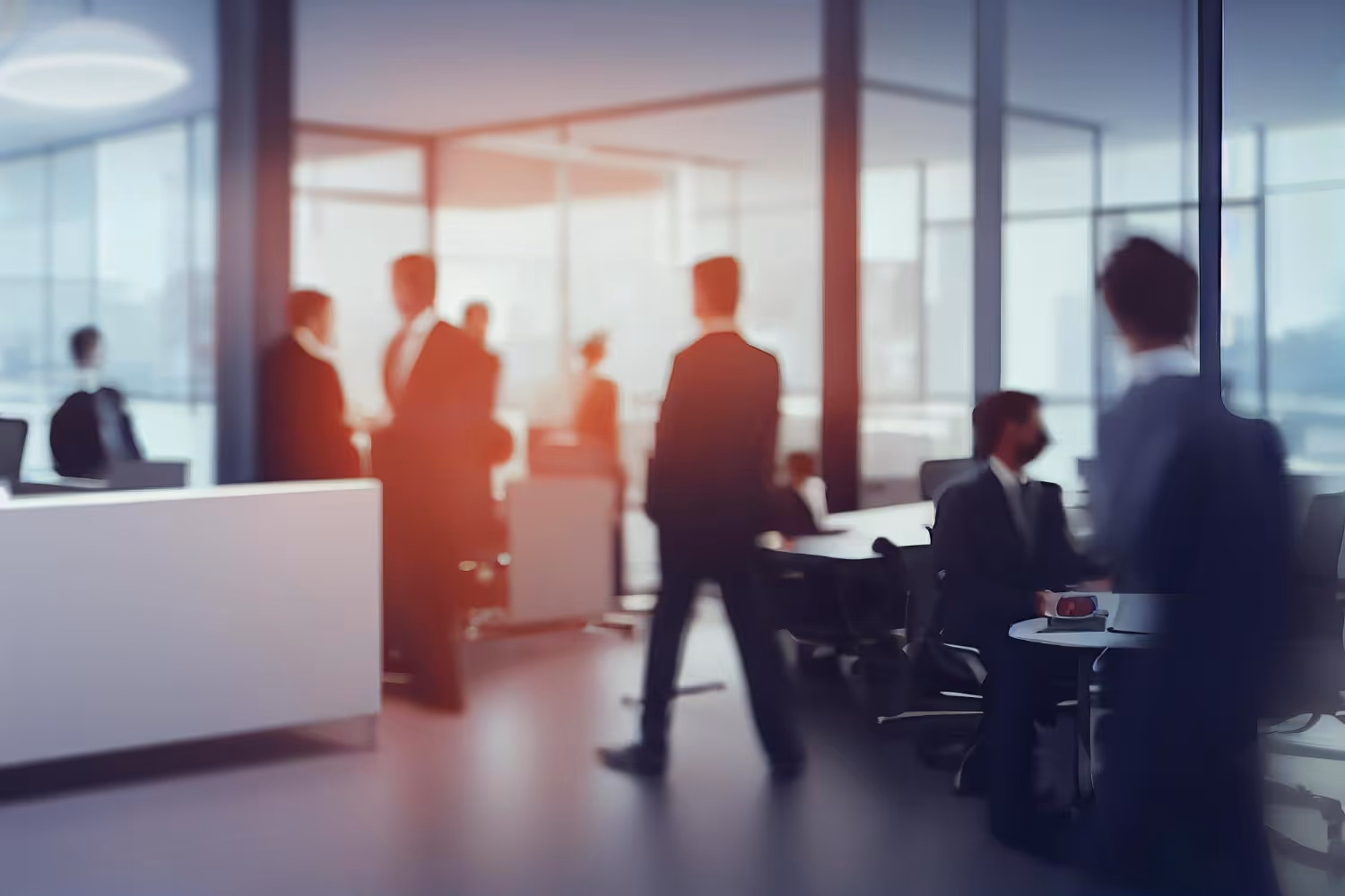 Blurred image of businesspeople in formal attire interacting in a modern office with large windows.