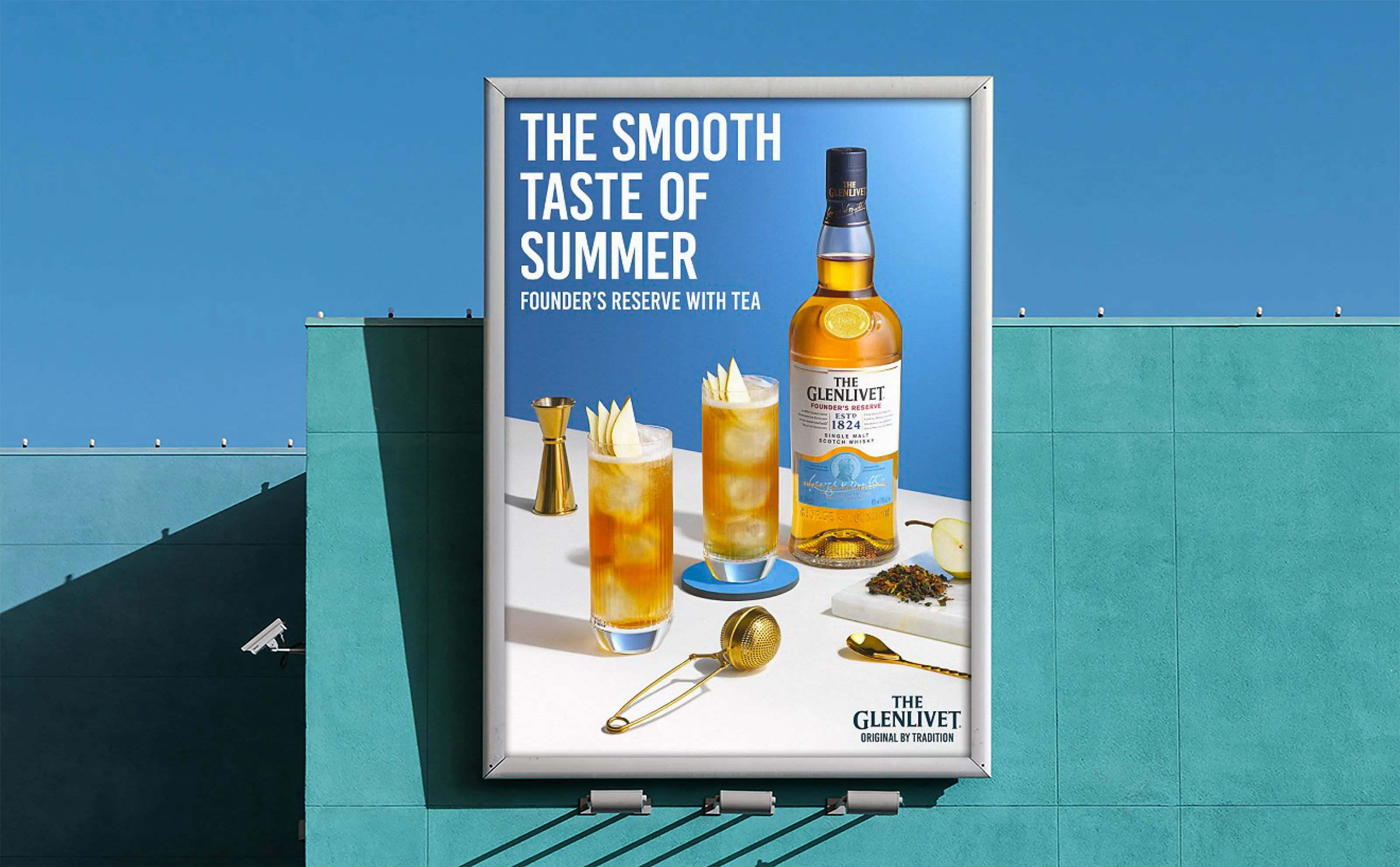 Billboard against a turquoise wall and clear blue sky advertising The Glenlivet Founder’s Reserve with tea, featuring a bottle of whisky, two glasses with ice and garnishes, a gold jigger, tea leaves on a marble slab, a gold spoon, and a tea infuser.