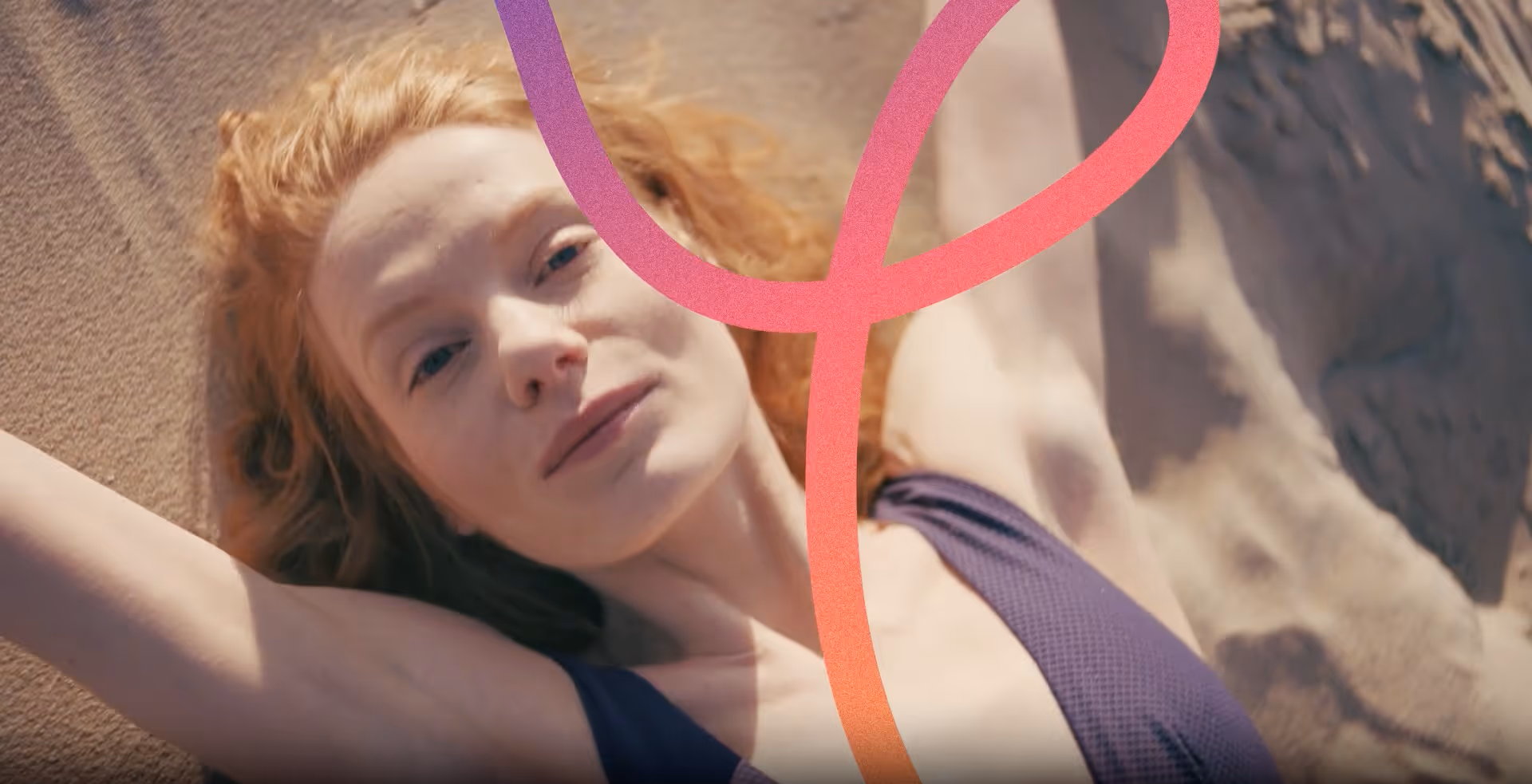 Vrouw met rood haar liggend op het zand met opgeheven armen en een paarse top.