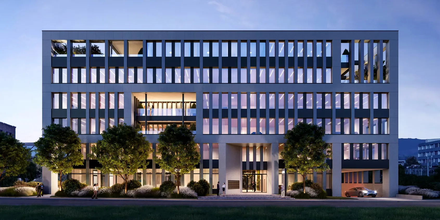 Modernes Bürogebäude mit großen Fenstern und beleuchteten Innenräumen bei Abenddämmerung, umgeben von Bäumen und Pflanzen.