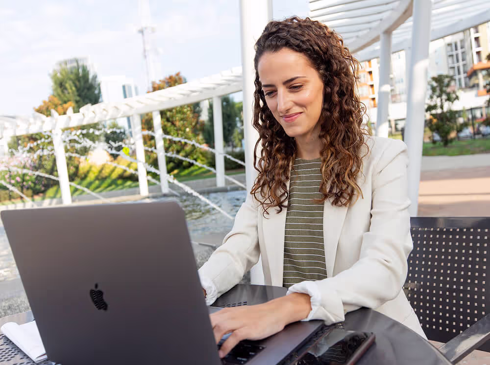 A female student typing on a laptop in a bright outdoor setting.
